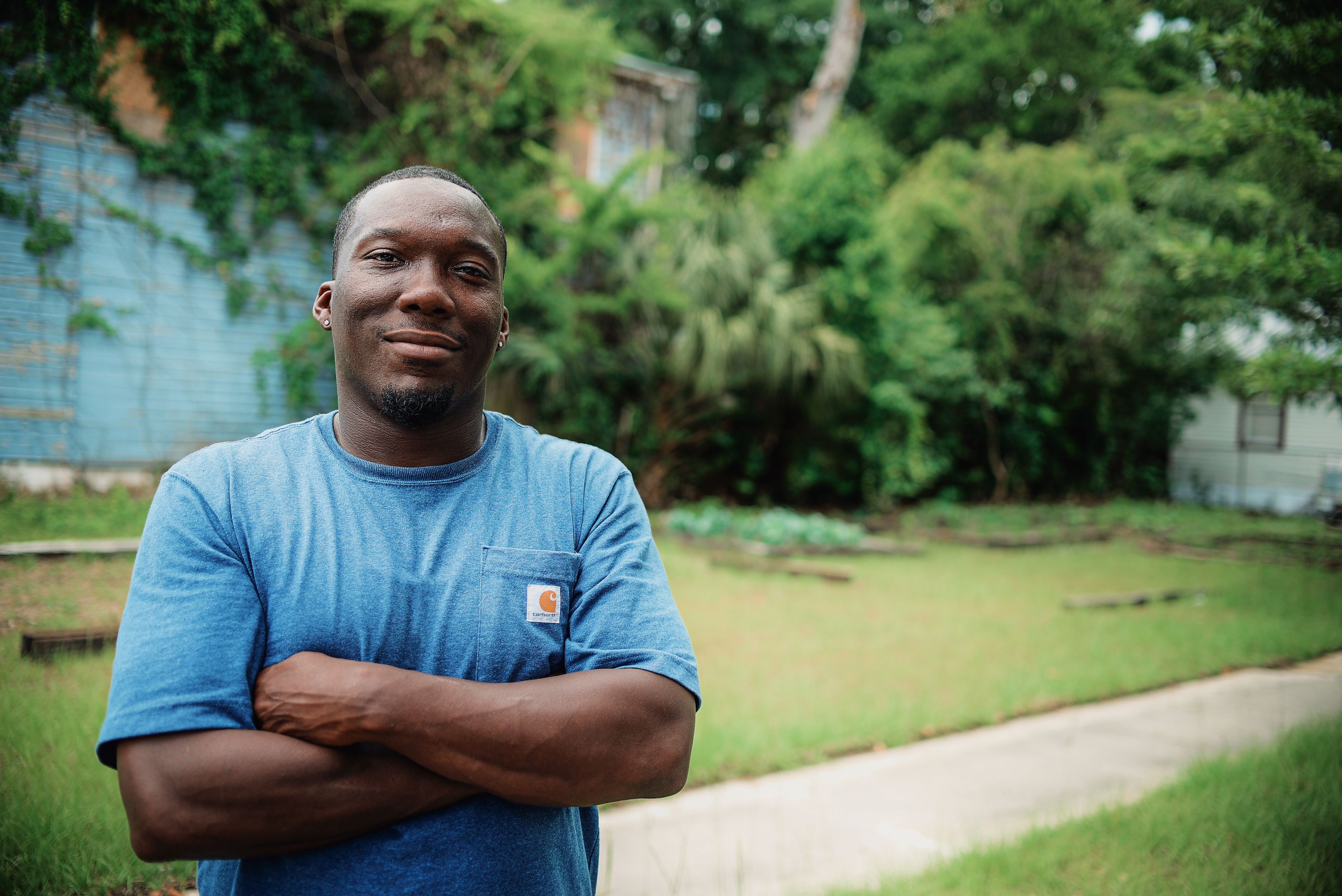 Wearing a blue Carhartt t-shirt, Edwin Thomas smiles while standing in the community garden in Savannah