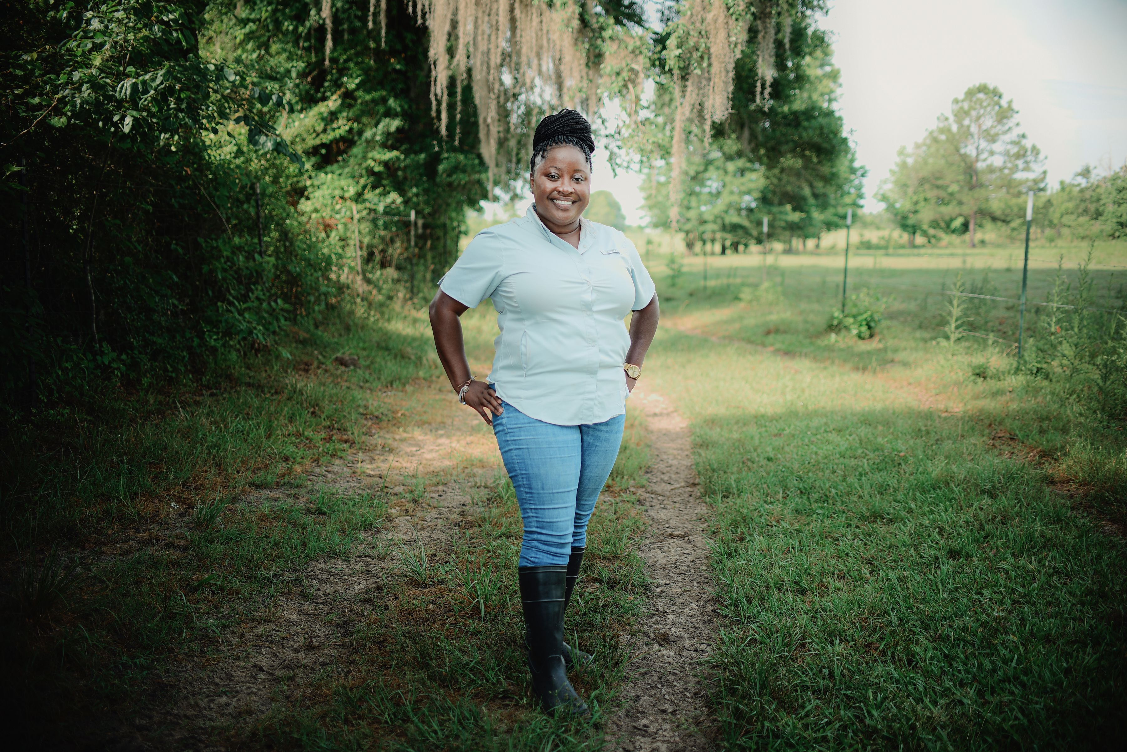Leslie Weaver Thomas smiles with her hands on her hips on a dirt road with Spanish moss hanging overhead