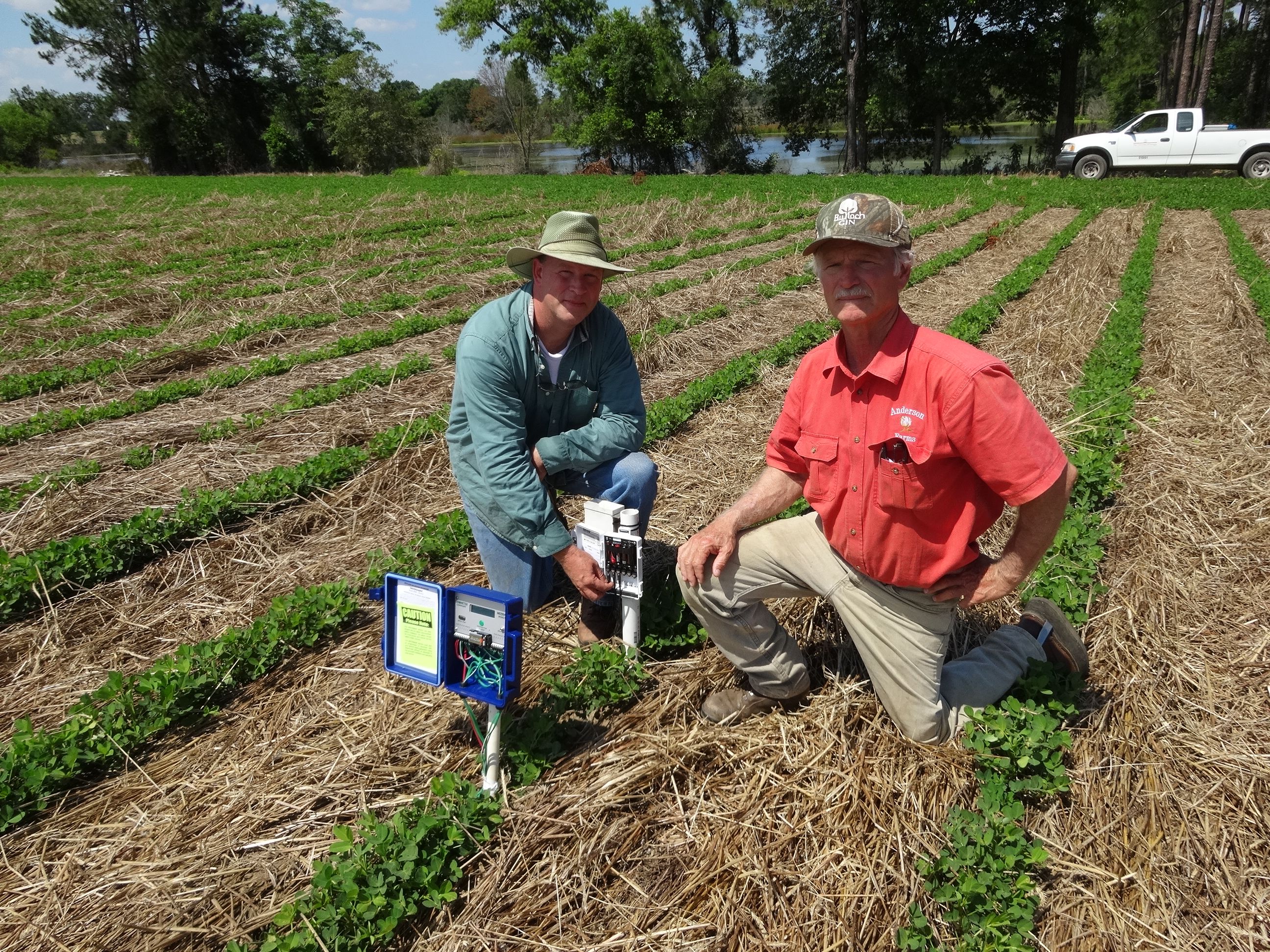 Two men kneel as they install equipment in an agricultural field