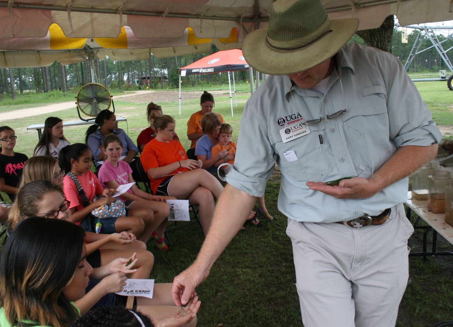 Hawkins presents to a group of young students under a tent at Stripling Ressearch Park