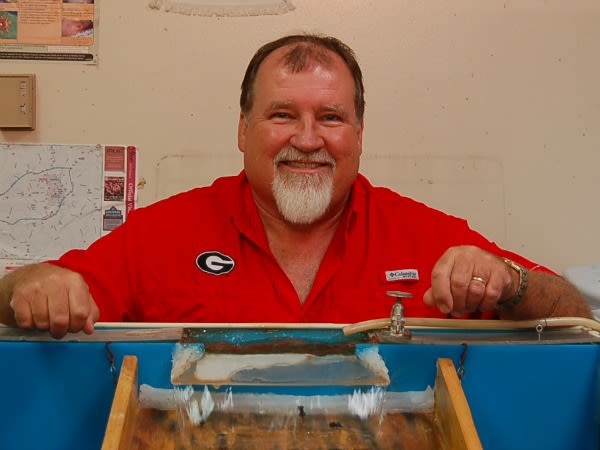 Gray, wearing a red UGA collared shirt, shows off one of the black fly rearing units in his lab.