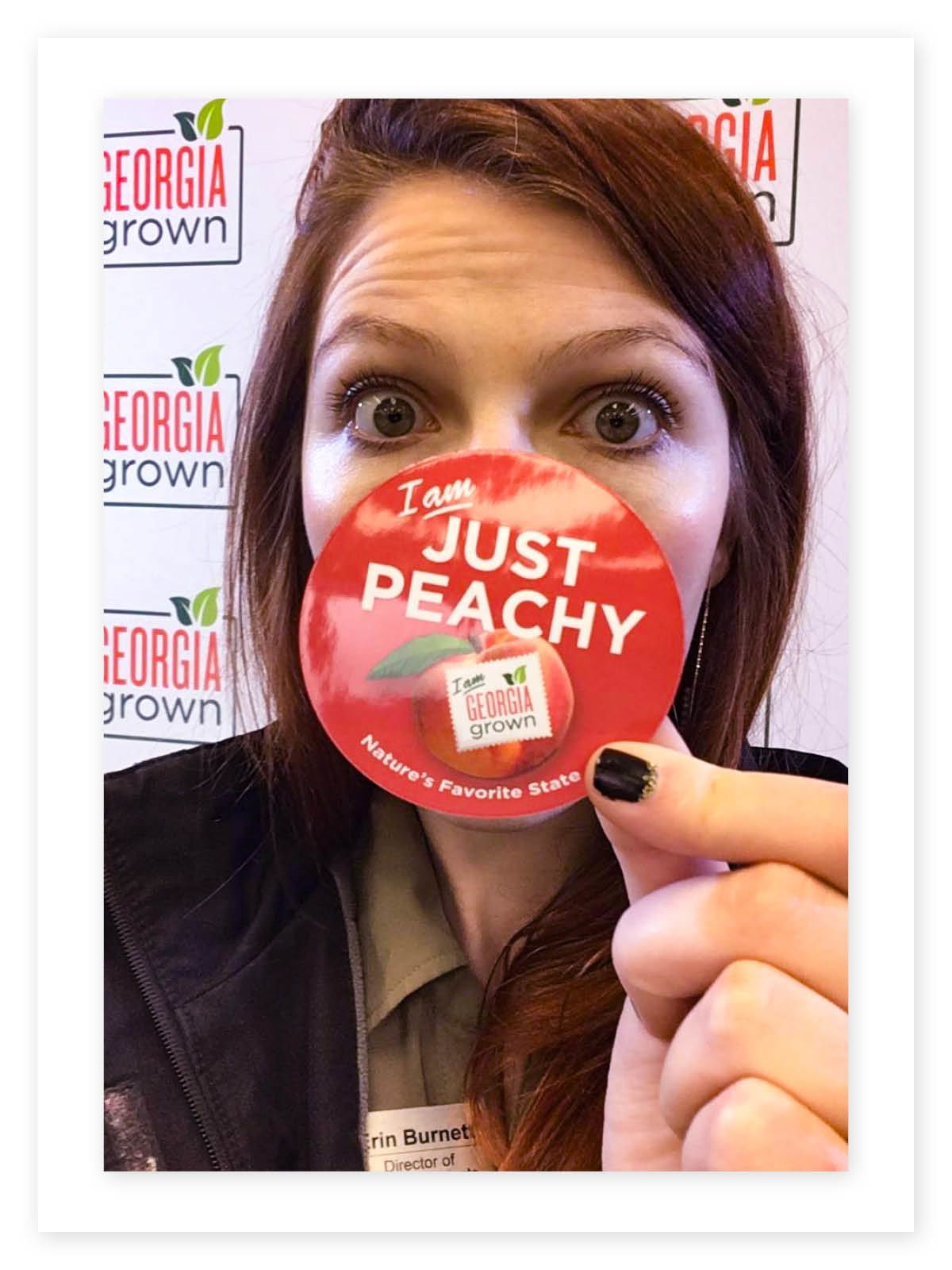 Woman holds a decorative pin that says "I am just peachy"