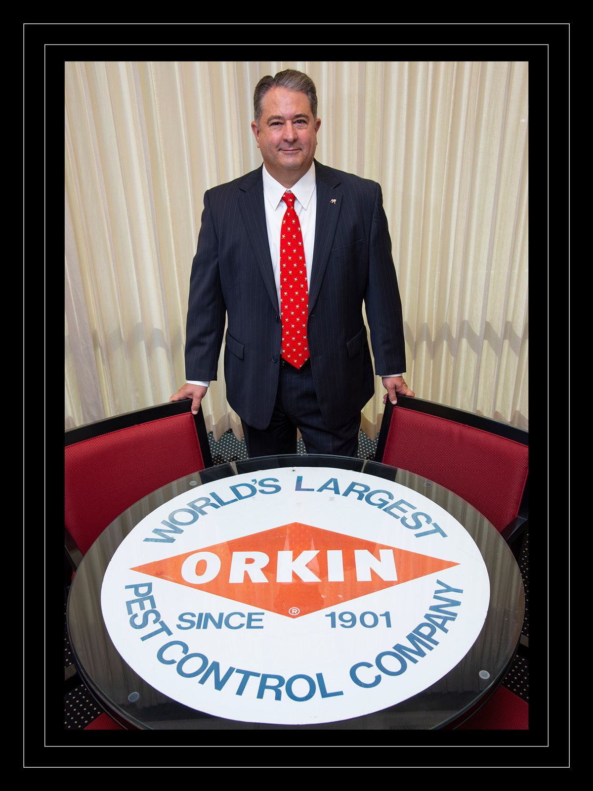 Man in suit stands in front of Orkin-branded conference table