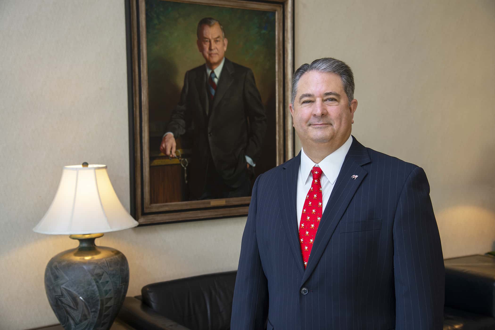 Man in suit stands in front of painting of another man in suit