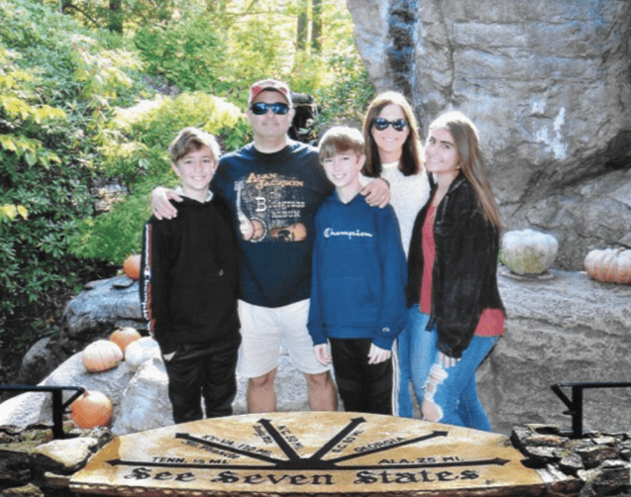 Elliott stands with his wife and three children in front of rocky wall and trees