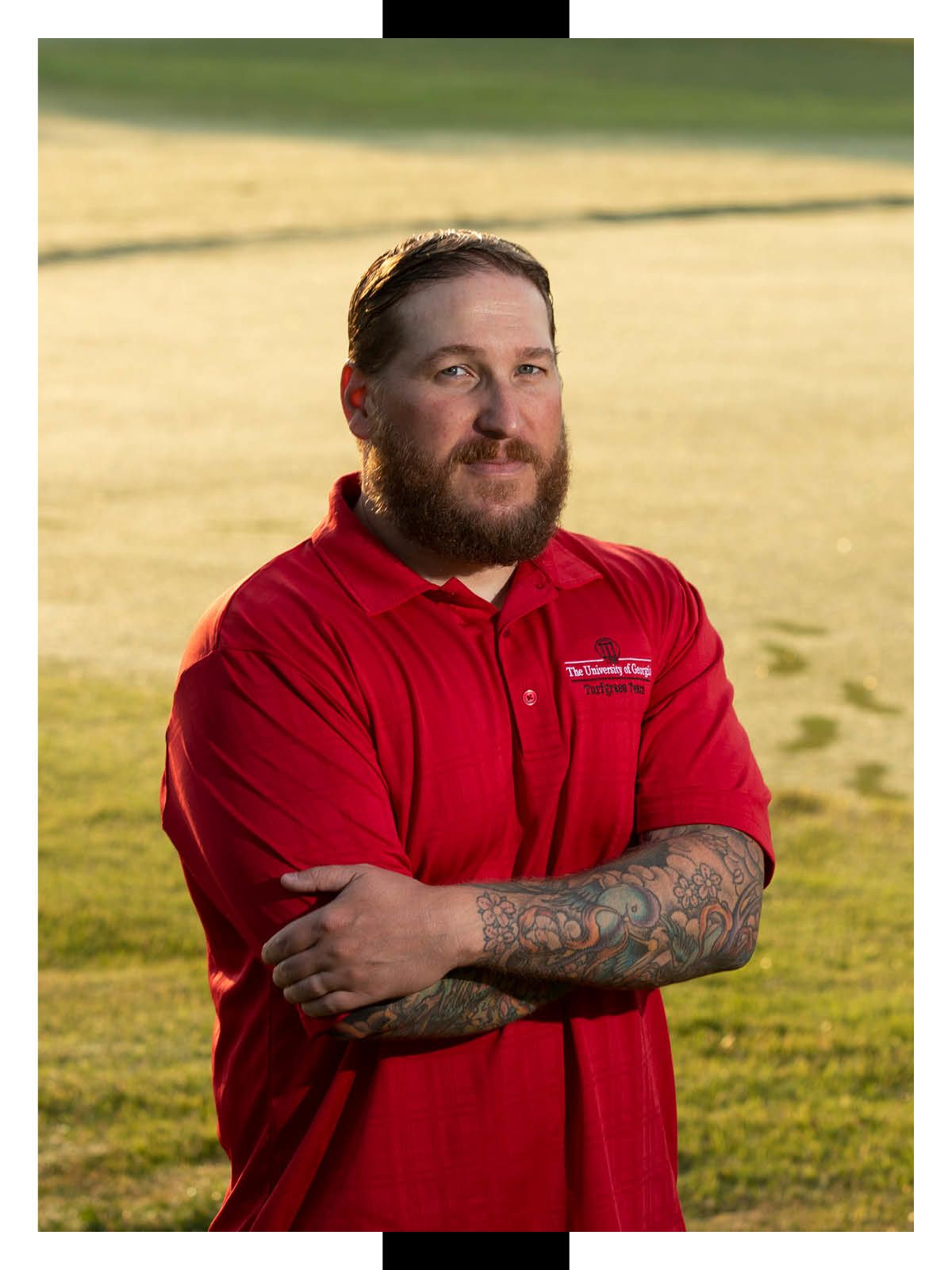 Gerald Henry stands in a field of turfgrass wearing a red collared shirt with University of Georgia Turfgrass Team embroidered on his left