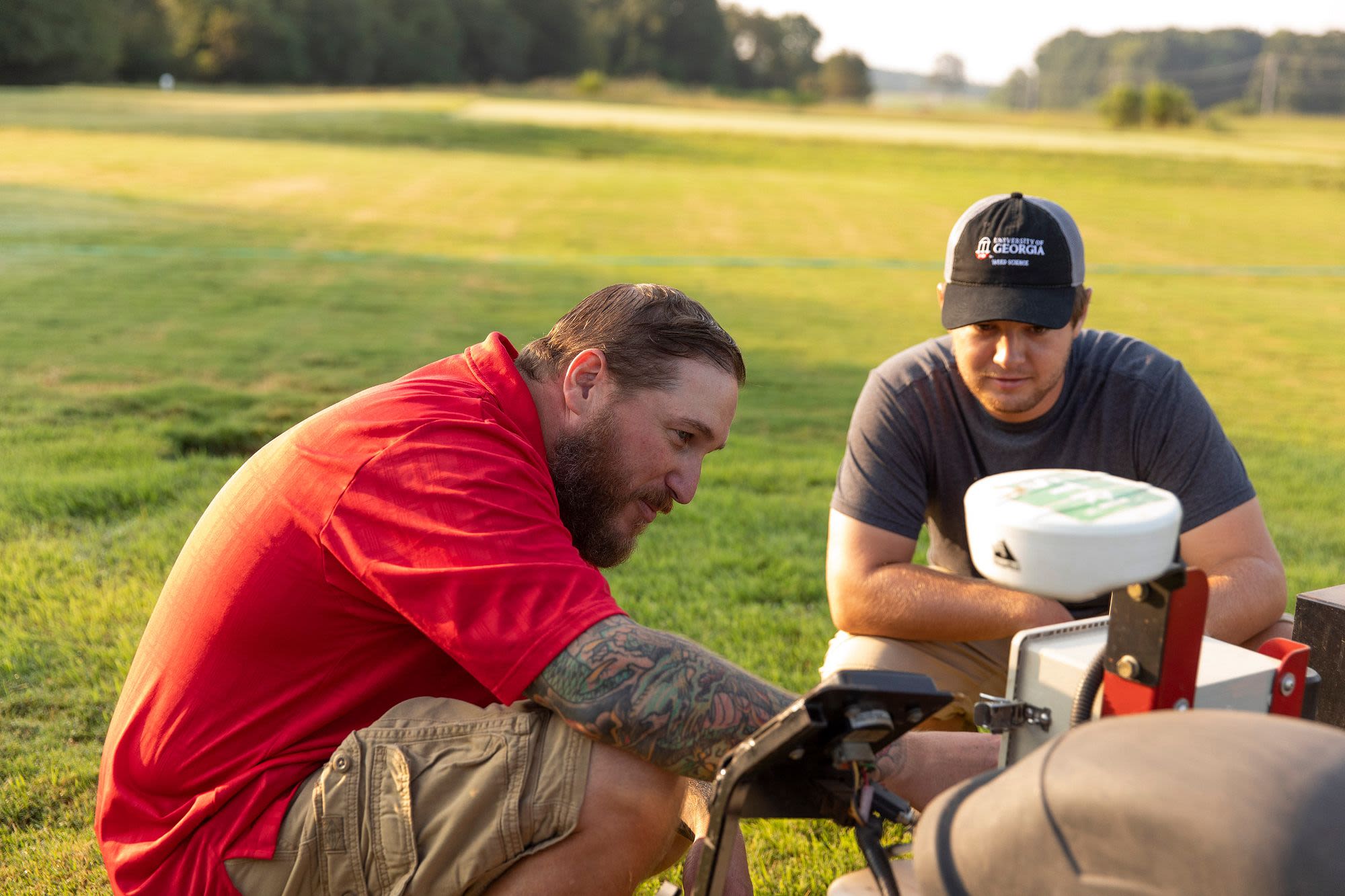 Two men work on a mower in a field