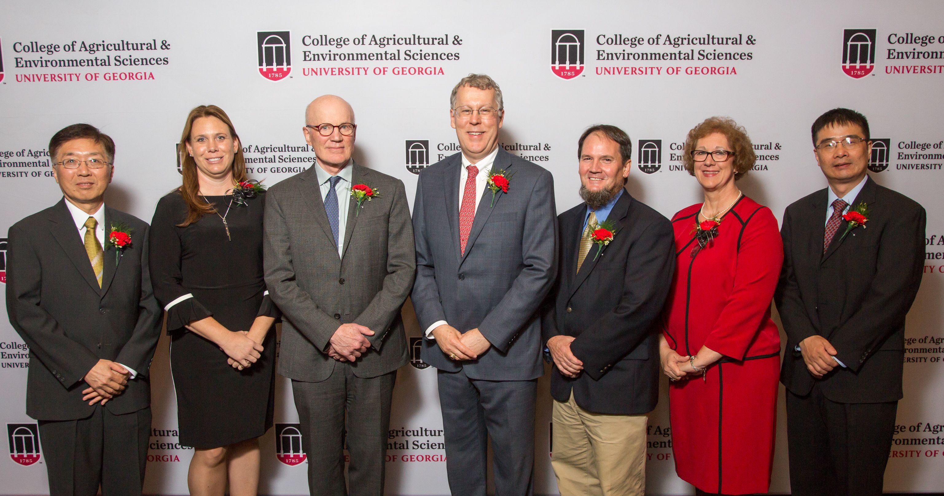 Seven people pose for a photo in front of a CAES logo backdrop