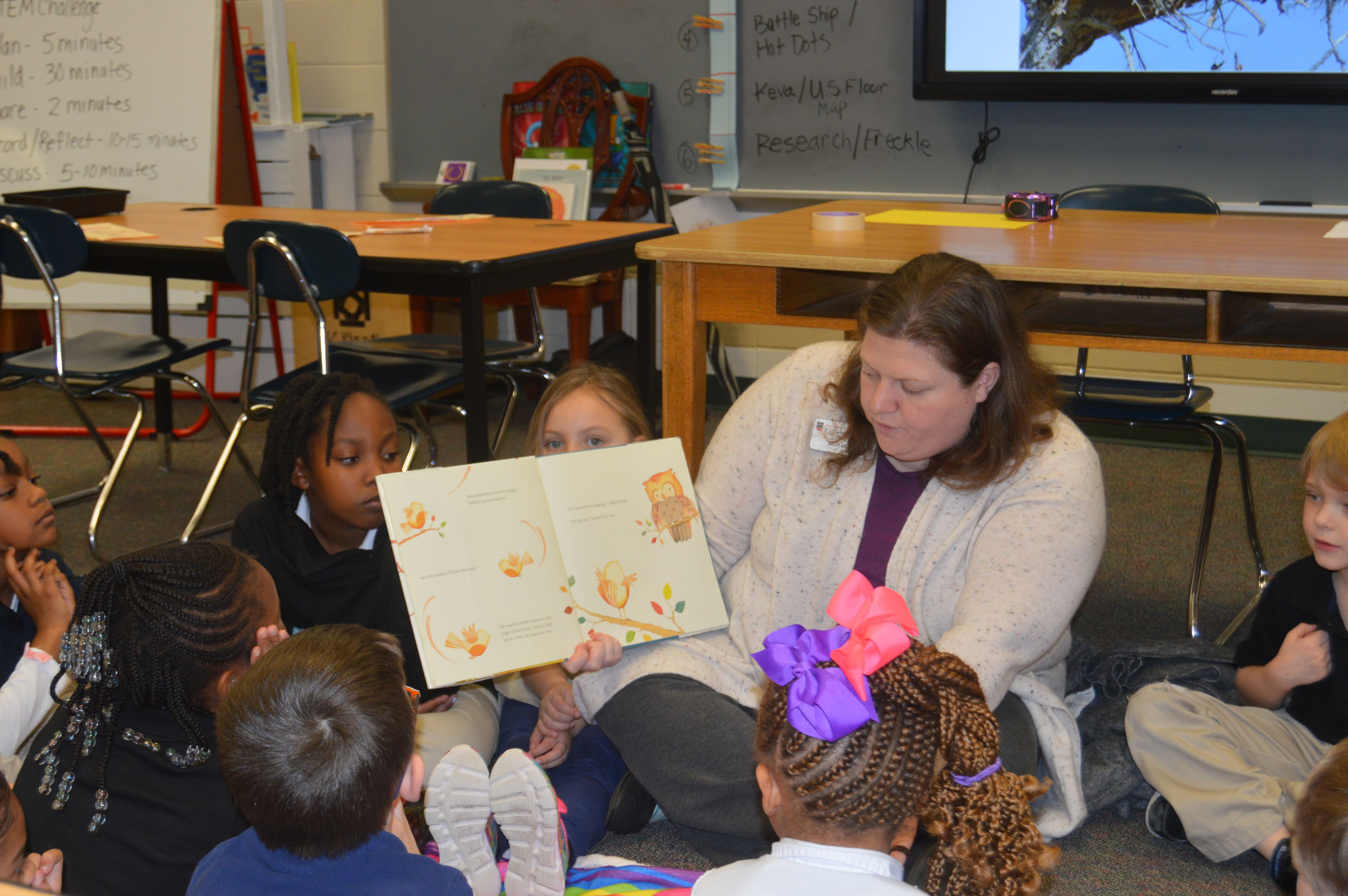 Kasey Bozeman reads to a group of children while sitting on the floor of a classroom