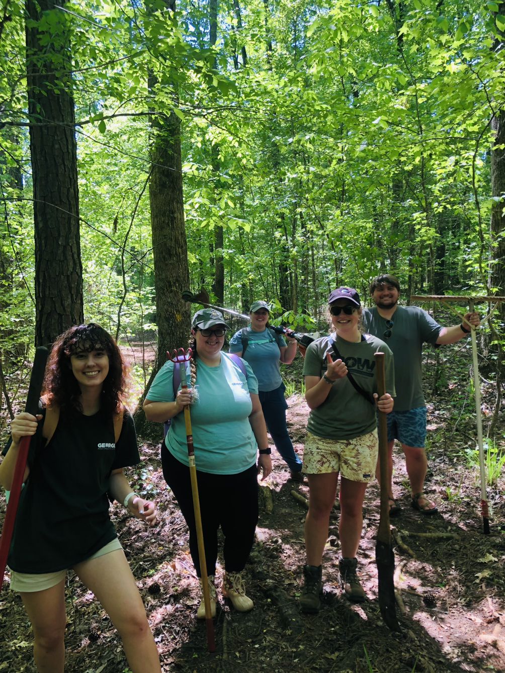 Swanger and four coworkers pose with clean-up gear on a trail at Rock Eagle 4-H Center