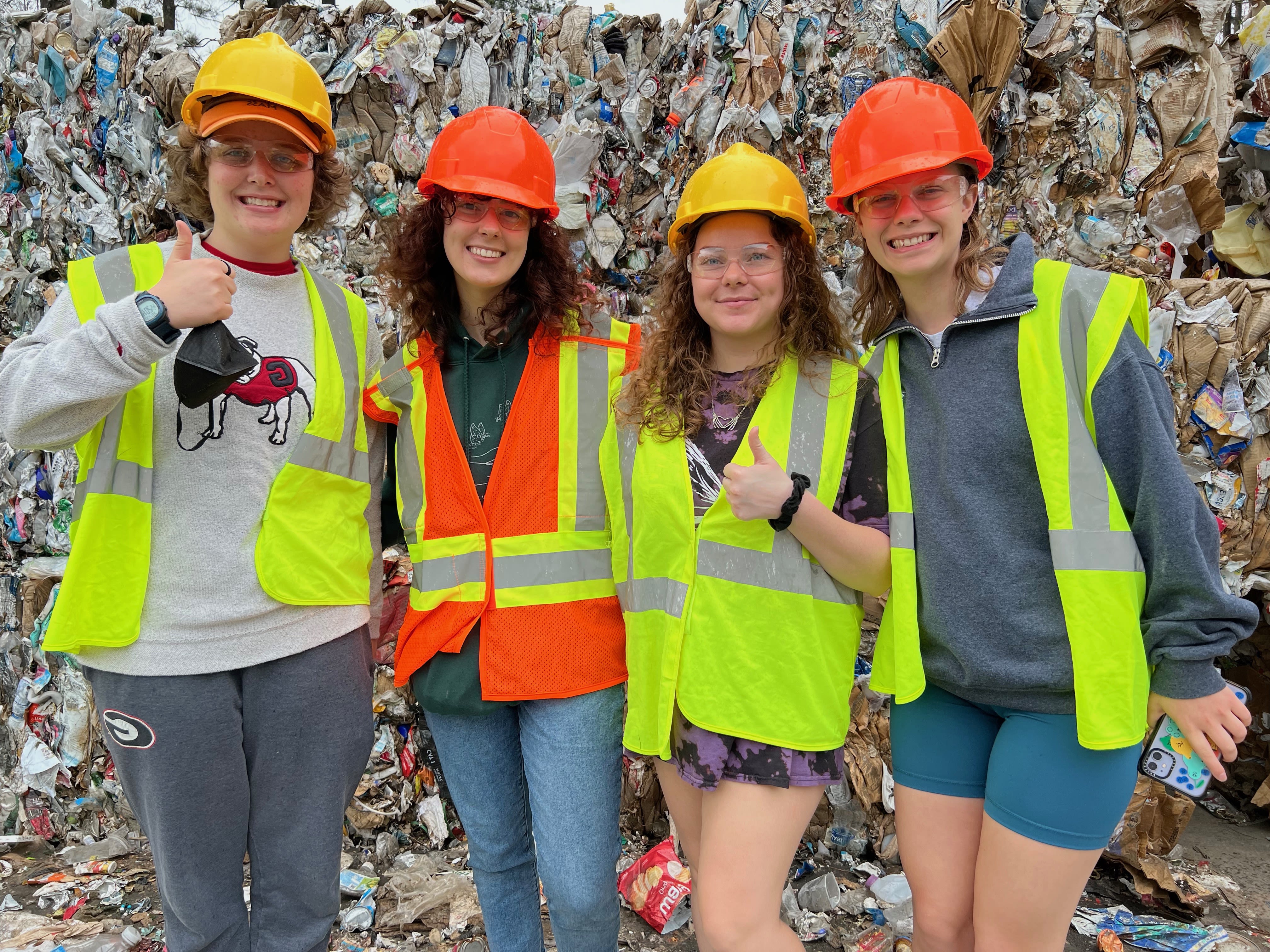 Wearing protective gear, Swanger and her classmates stand in front of a large trash heap