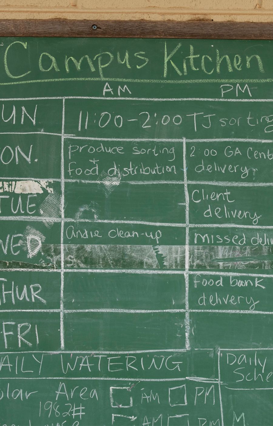 A chalkboard titled Campus Kitchen is covered in tables with a weekly schedule.