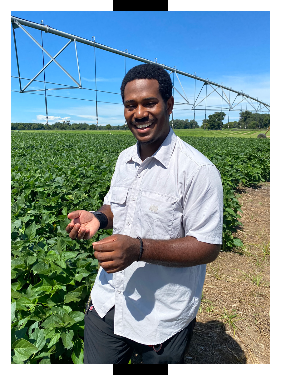 Jermaine Perier smiles while standing in a field. He is wearing a white button up shirt. There is a center pivot irrigation visible in the background.