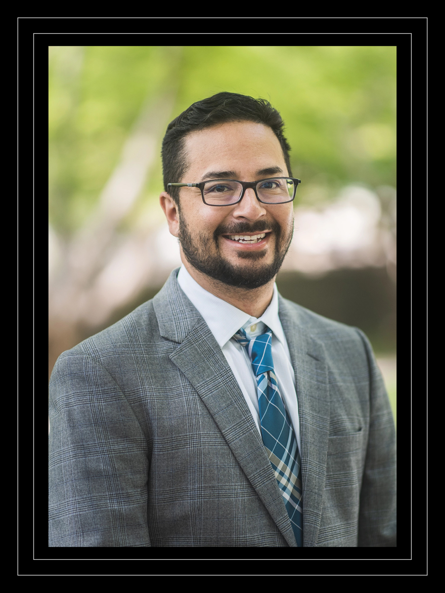 Associate Professor John Michael Gonzalez smiles while wearing a gray suit and plaid tie at the State Botanical Garden in Athens, Georgia