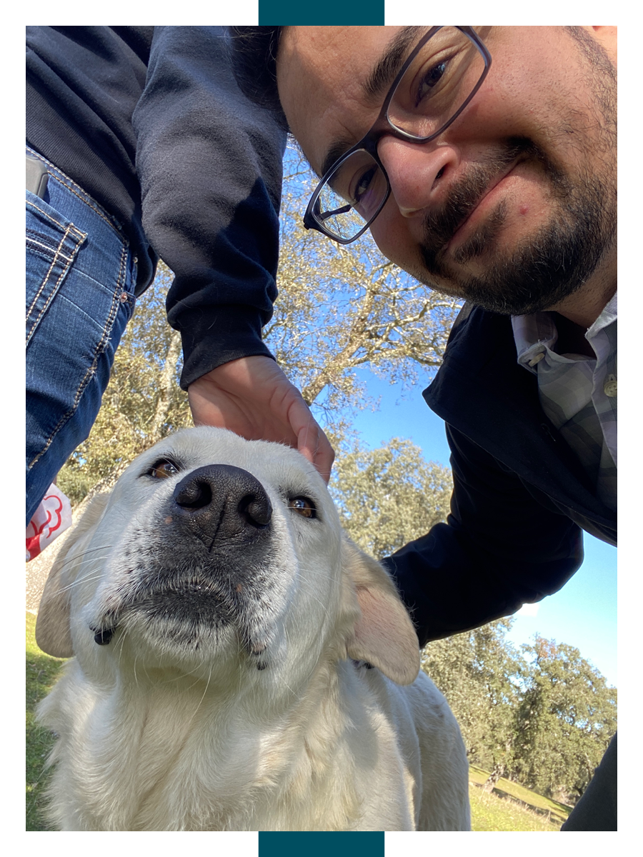 John Michael Gonzalez leans down to pet a light-colored dog whose nose is close to the camera