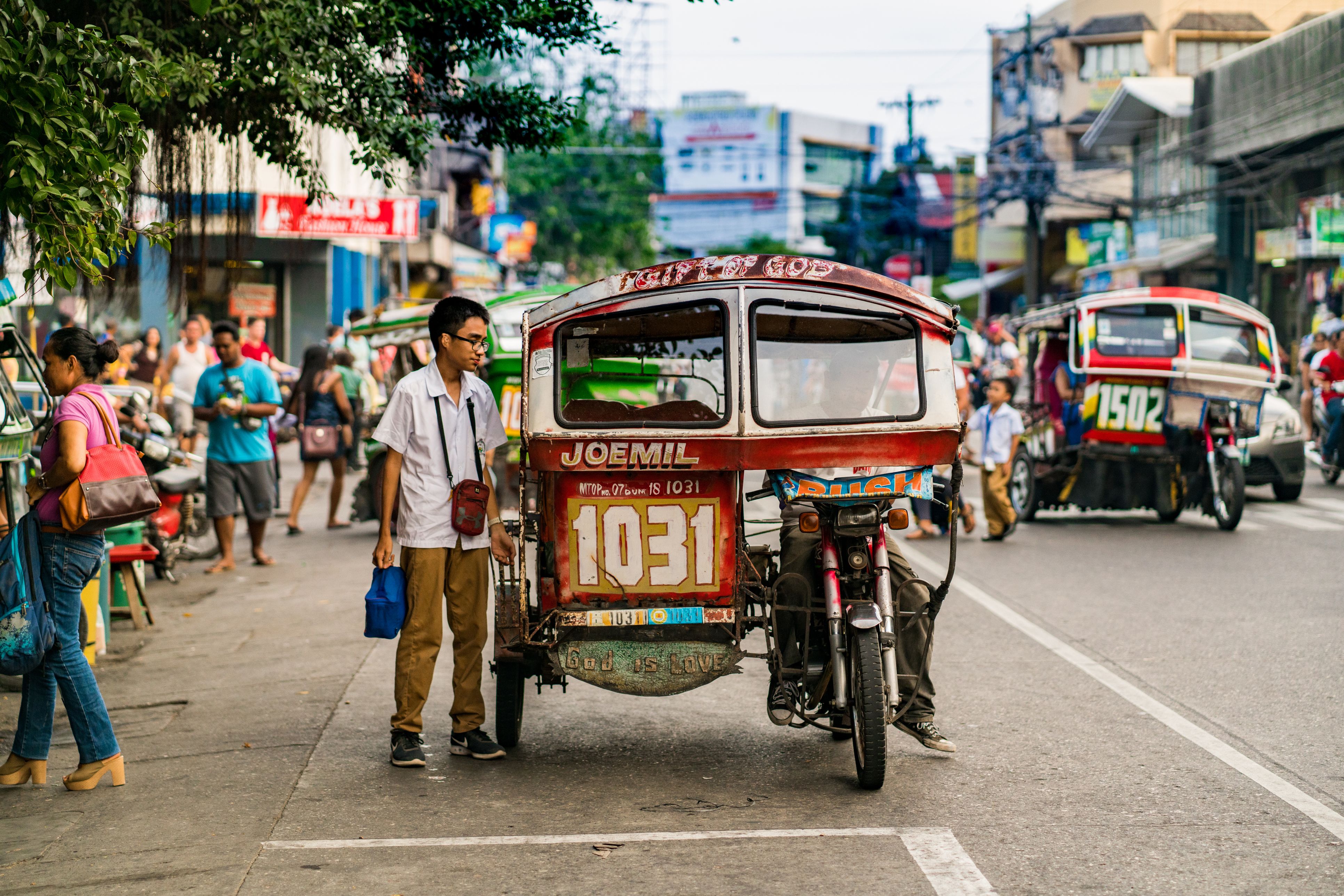 Negros Oriental view showing tricycles with passengers and pedestrians on the street in the Dumaguete area with people on the background