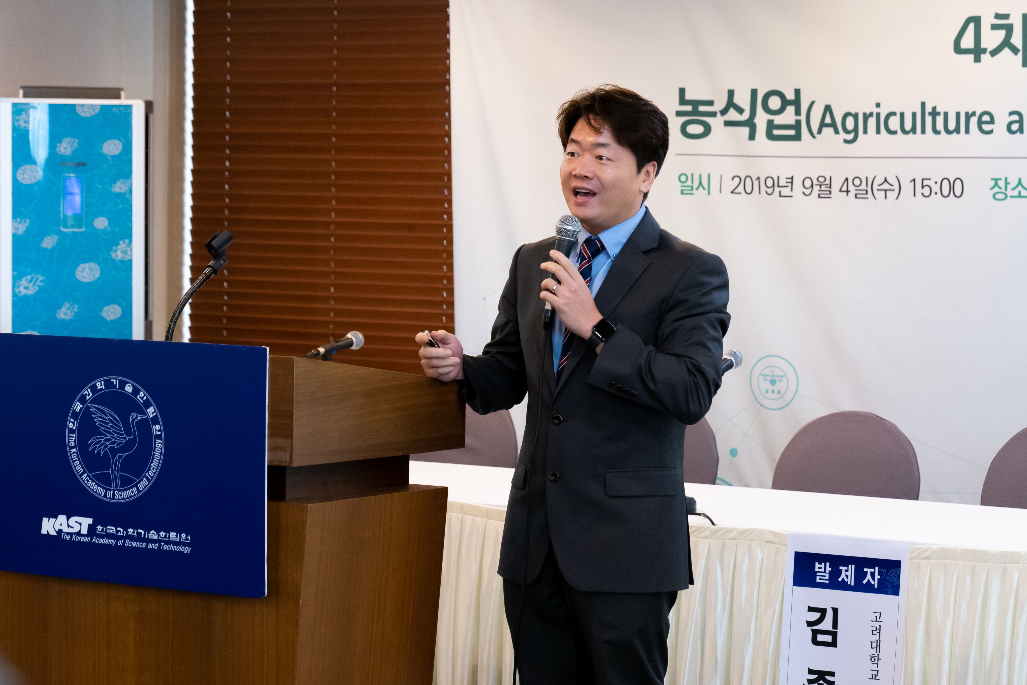 Jongyun Kim stands at a Korean Academy of Science and Technology-branded lectern with a microphone speaking on “The 4th Industrial Revolution and Agriculture.”