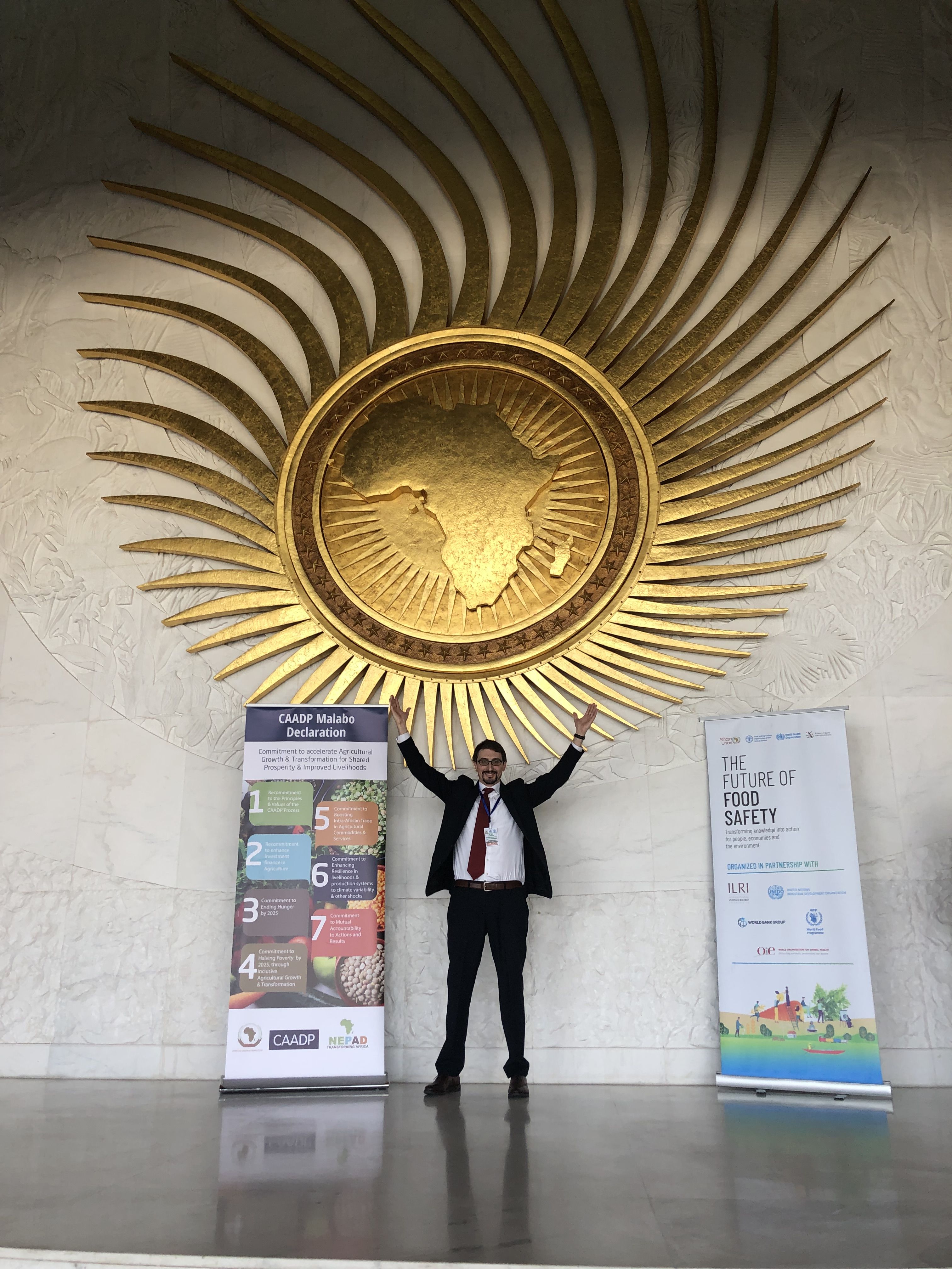 Lee Gross poses under a large gold globe medallion at the African Union Food Safety Conference in Addis Ababa, Ethiopia.