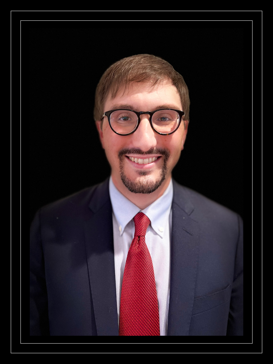 Lee Gross smiles while wearing a blue suit and red tie