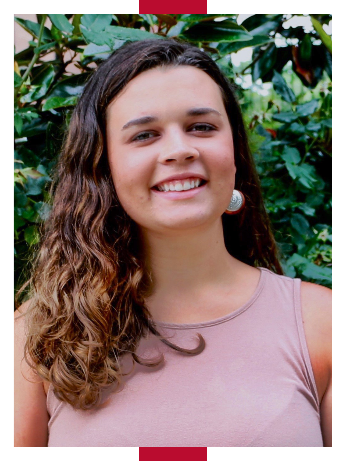 In her headshot, UGA student Marin Lonnee smiles in front of greenery while wearing a light purple sleeveless shirt and earrings