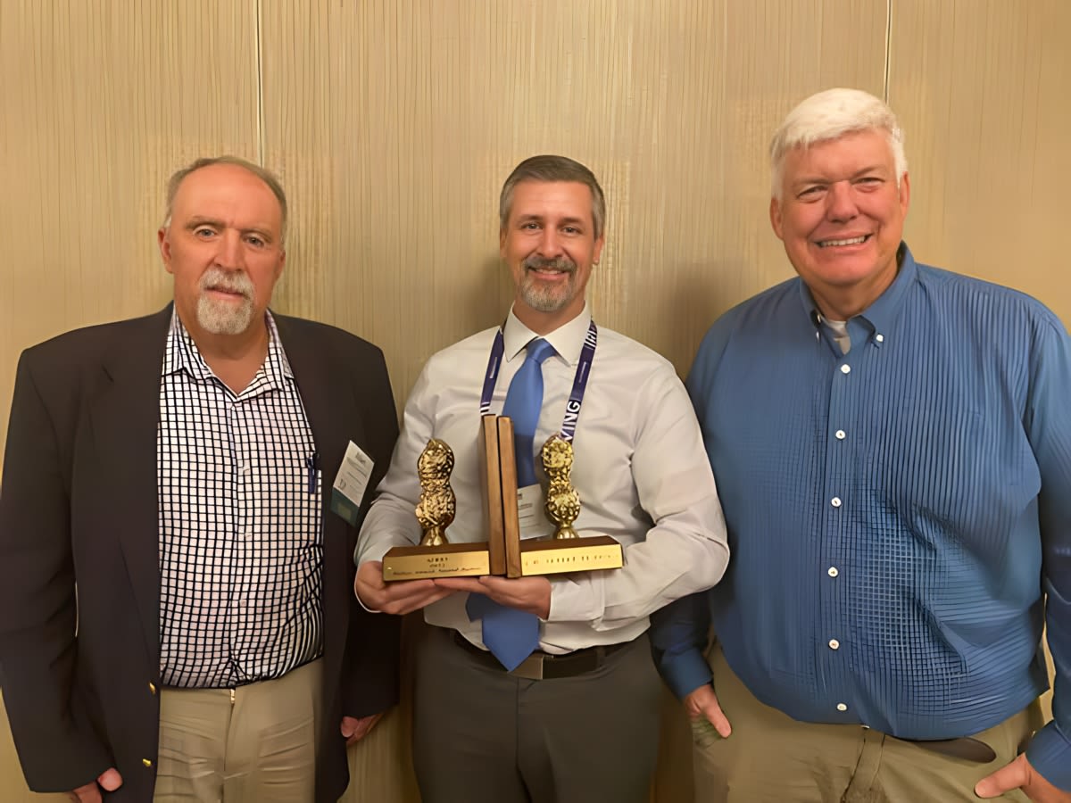 Three men pose for a photo holding a pair of golden peanut bookends