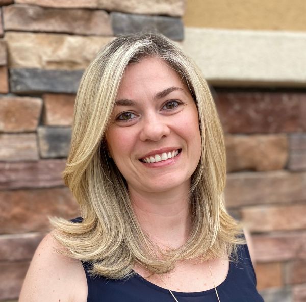 Cristiane Pilon stands outside in front of a stone wall in her professional headshot