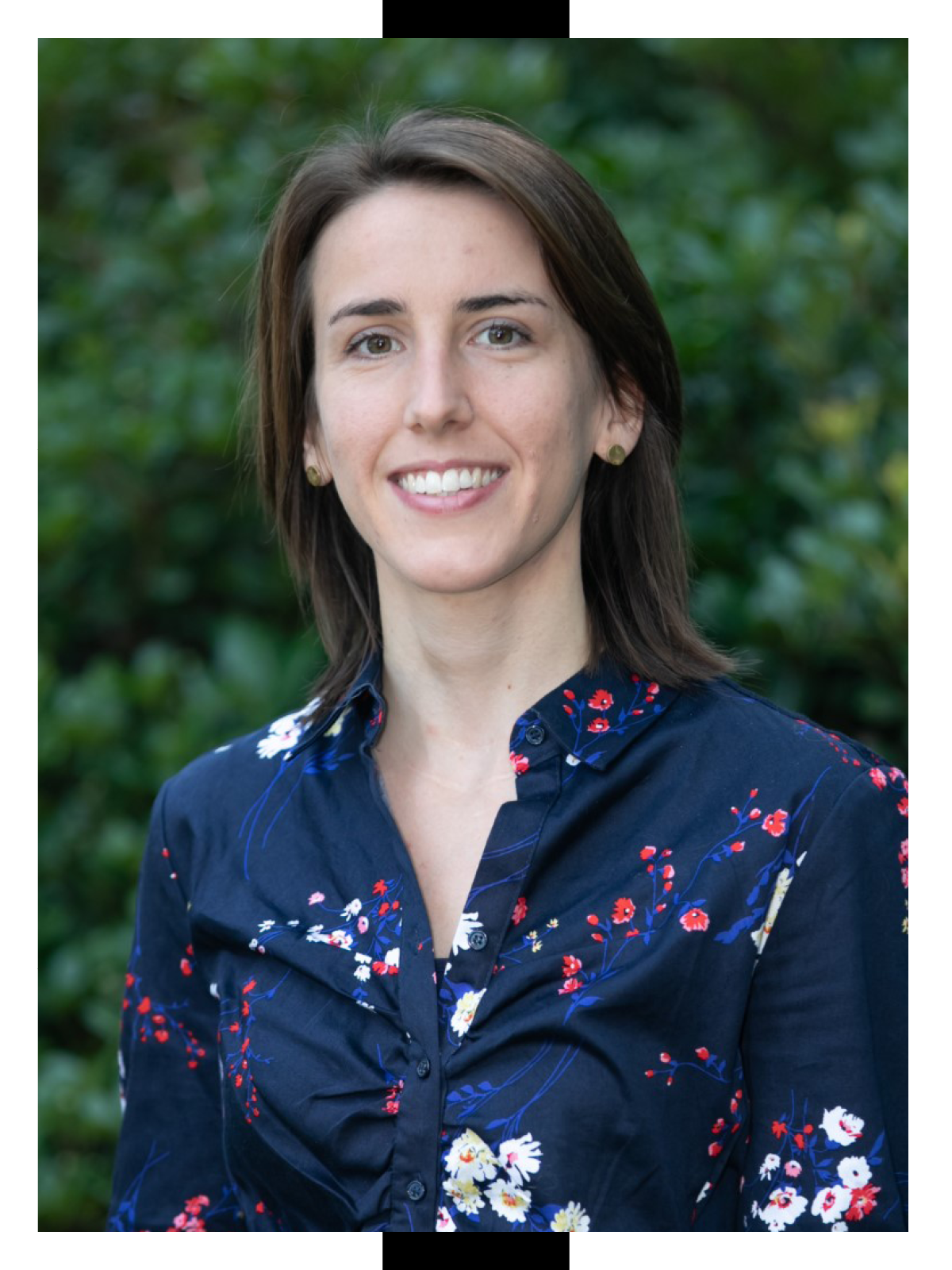 Laura Ney smiles in front of a background of greenery while wearing a naby floral button-up shirt