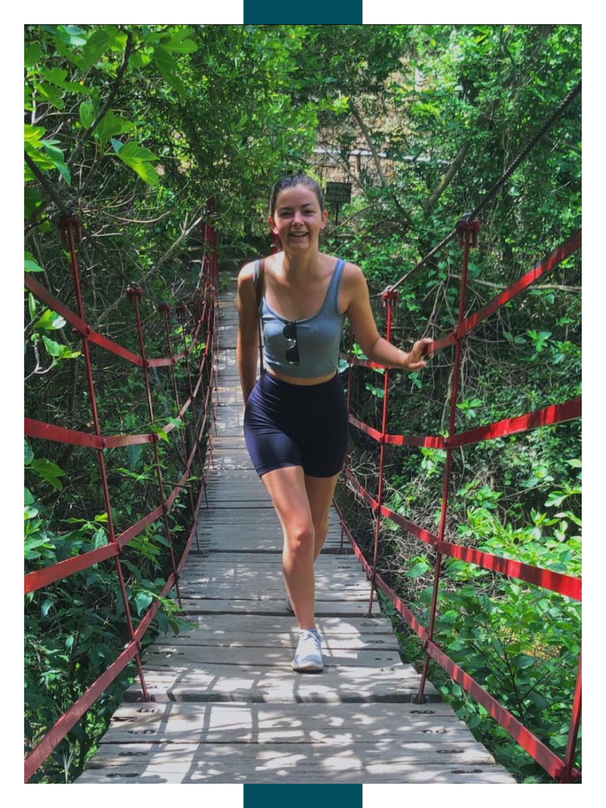 Lauren Bray faces the camera while crossing a foot bridge with red rails. 