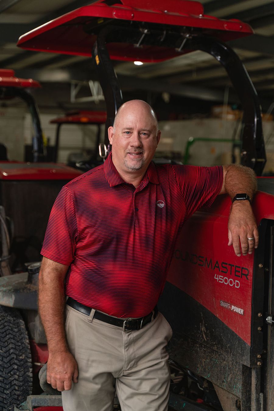 Jim Evans, in a red polo shirt, leans against a machine in an indoor workshop, with other equipment visible in the background.