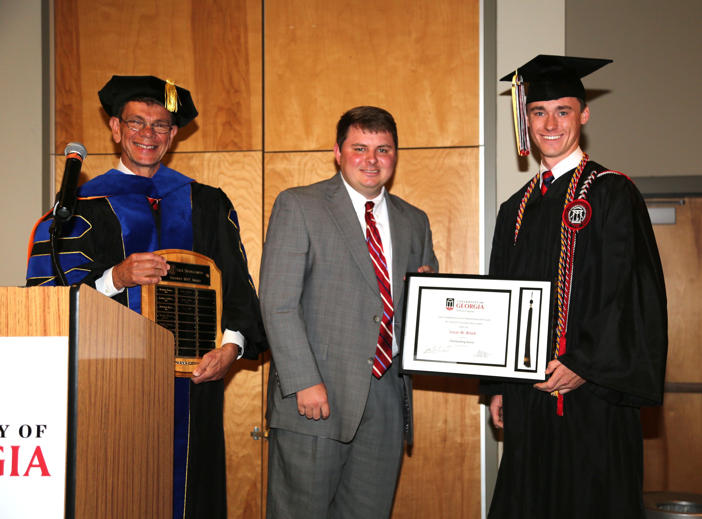 Lucas Brock smiles at the camera in his cap and gown while being presented an award.