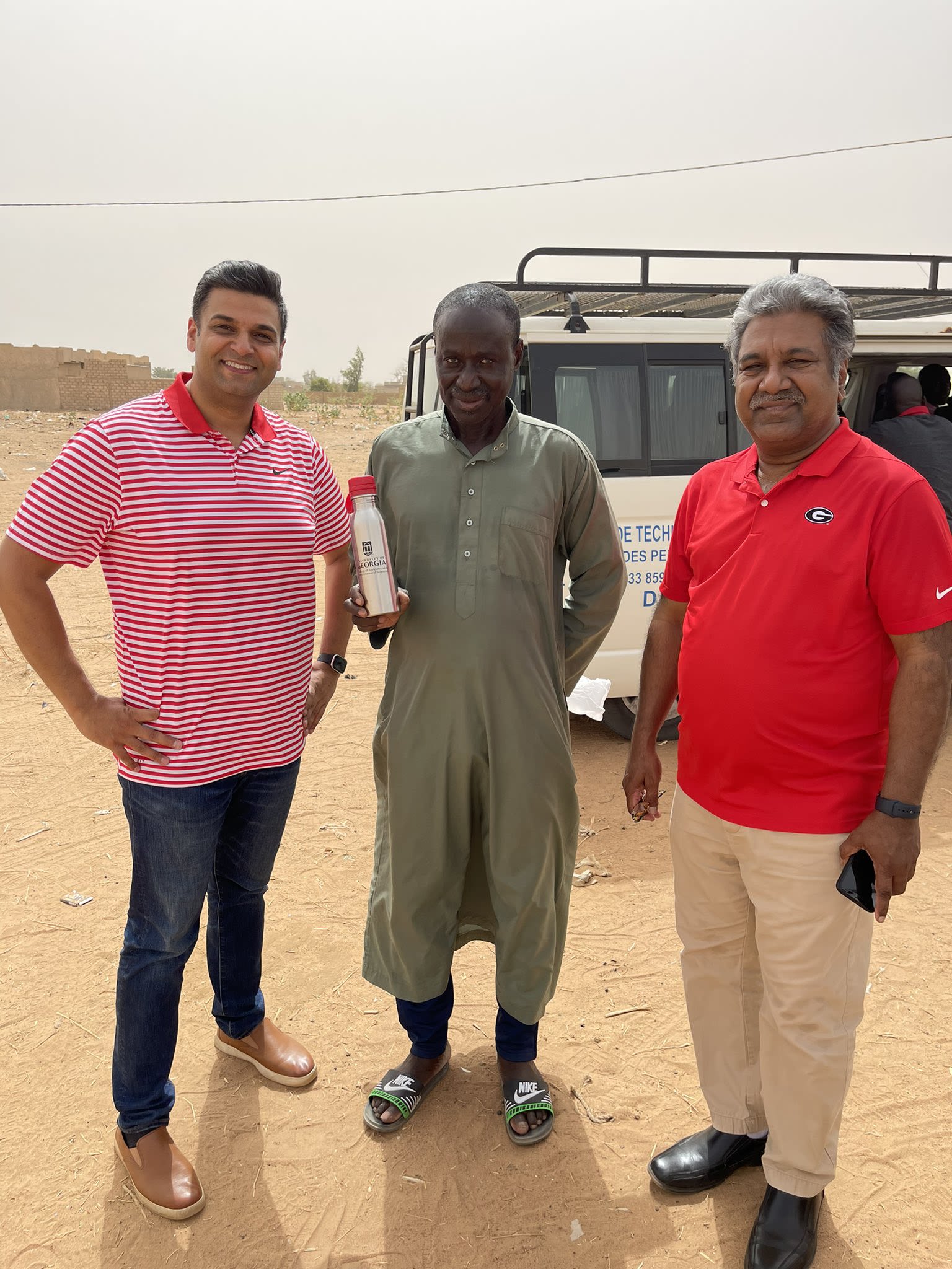 Manpreet Singh and Harsha Thippareddi wear UGA gear with a collaborator, who's holding a UGA water bottle, outside of a truckin Senegal