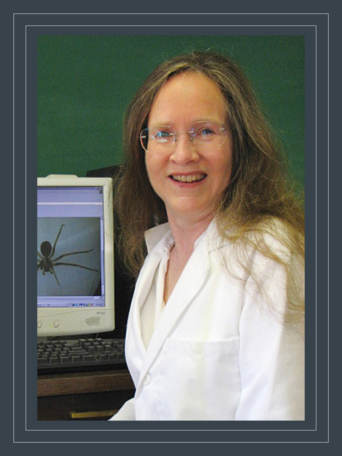 Nancy Hinkle wears a lab coat and sits in front of a computer with a spider on the screen