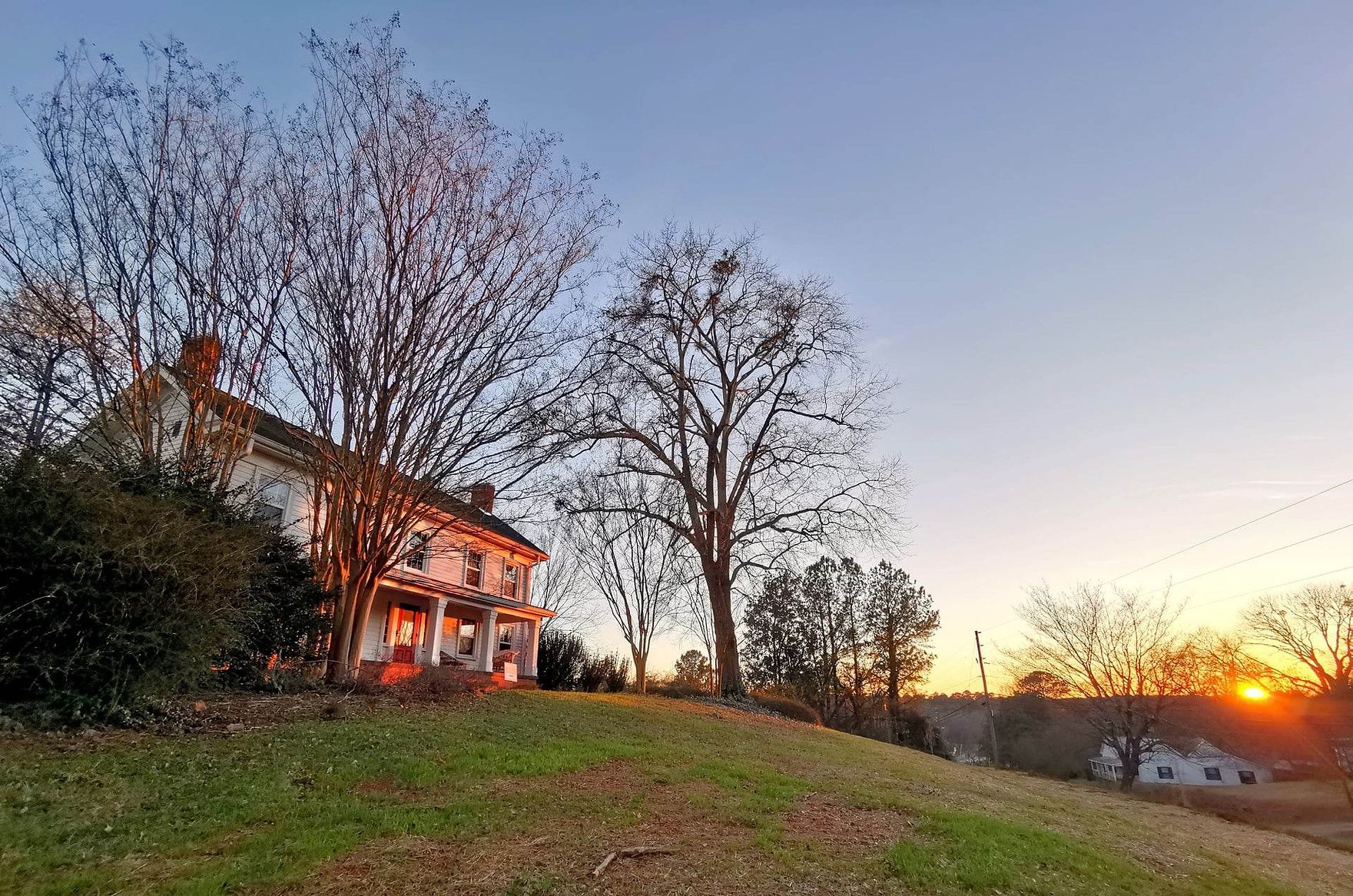 a landscape of Oak House Distillery's exterior with the sunset reflecting in the windows of the house.