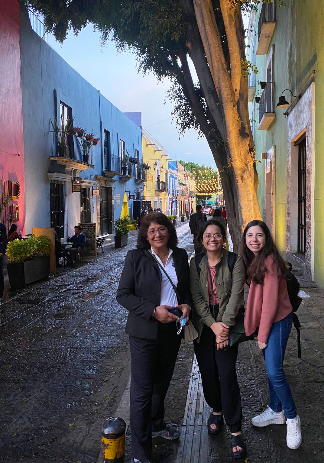 Raad stands with her advisor and her fellow exchange student on the streets of Mexico, with colorful buildings and string lights in the background