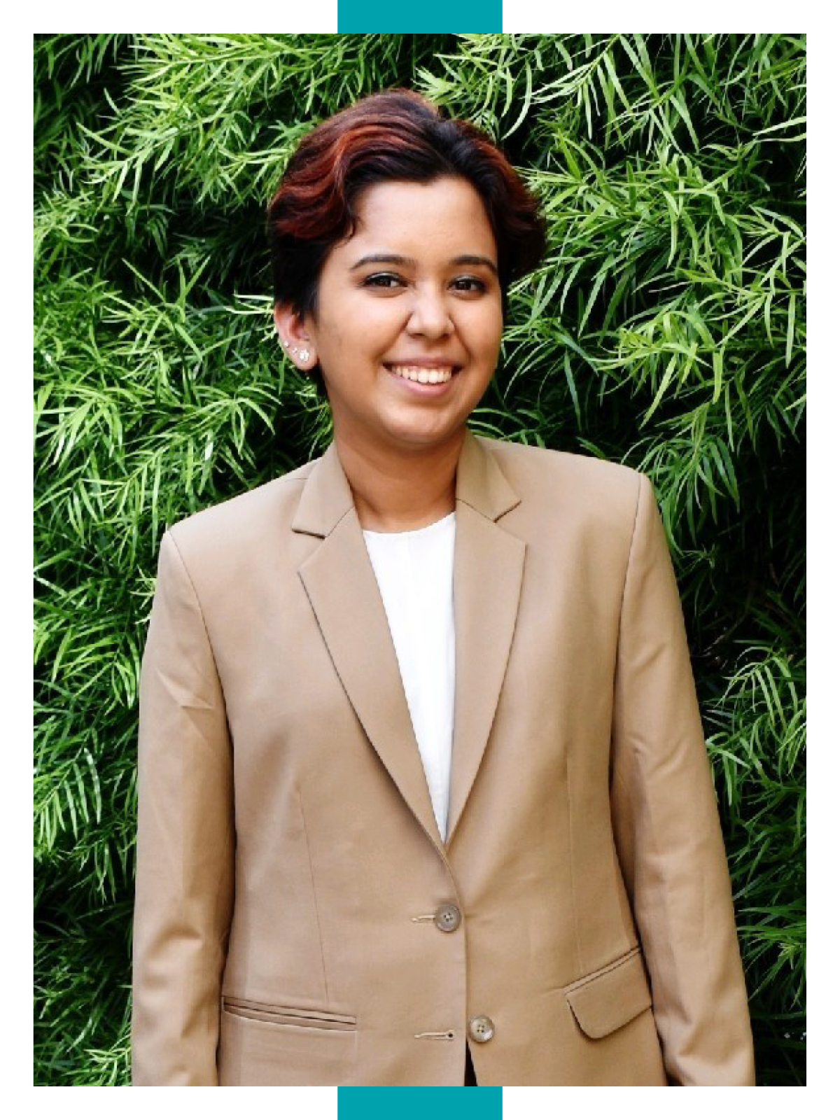 Revati Narwankar wears a khaki suit jacket and stands in front of a large shrub