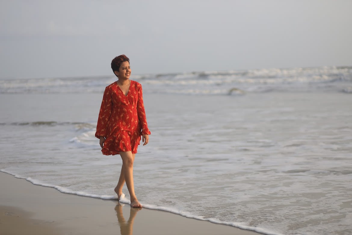 Narwankar walks along the beach in a short, red dress