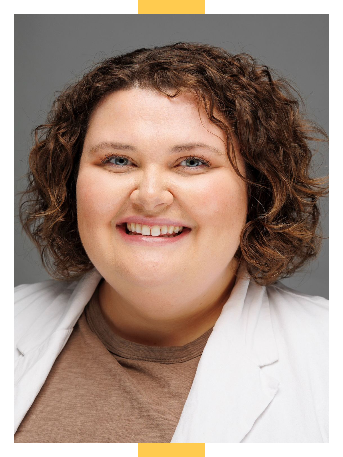 Sadie Lackey gives an open-mouthed smile while wearing an unbuttoned white blouse over a brown shirt in front of a dark grey background.