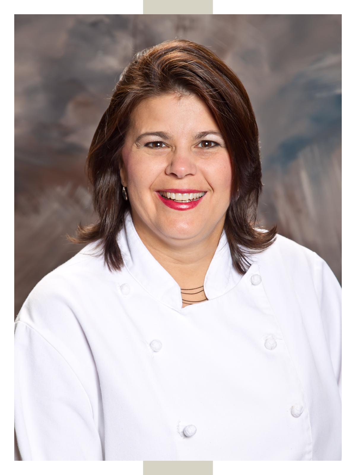 Shona Johnson wears her chef coat while smiling against a marbleized backdrop in her professional headshot