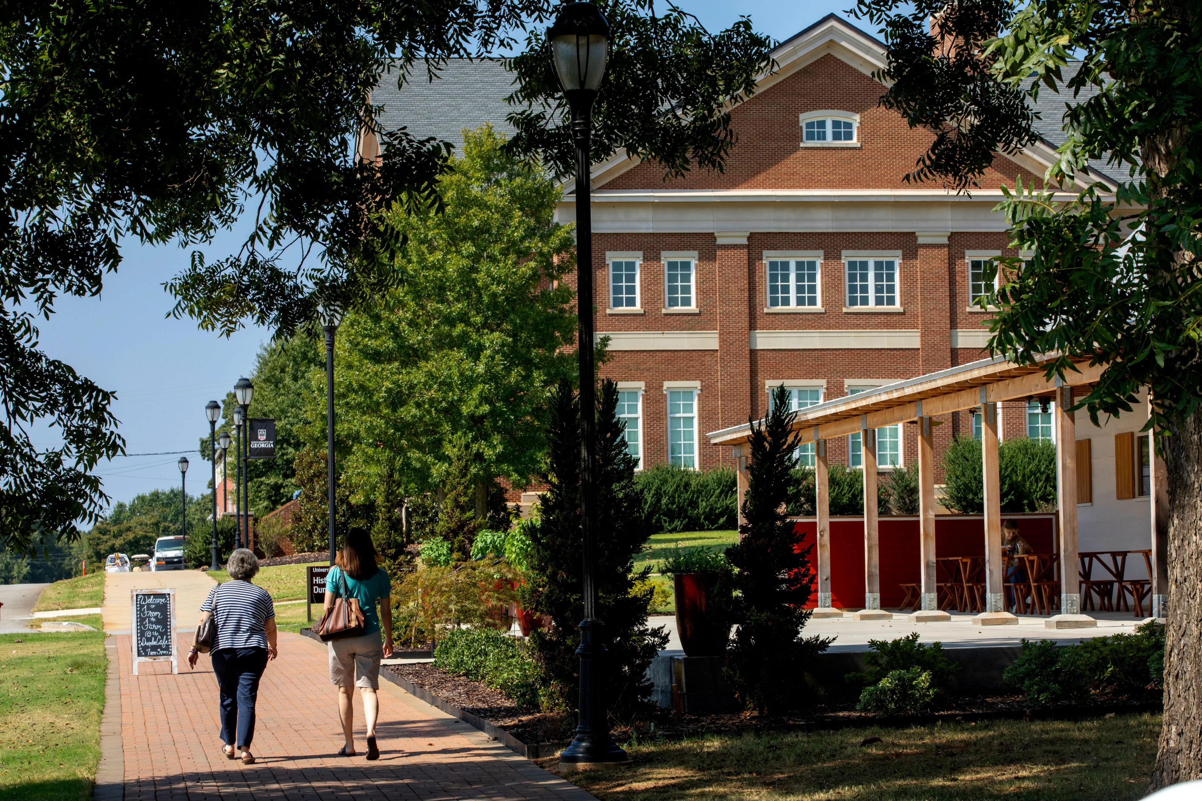Pedestrians walking on the sidewalk in front of the Student Learning Center and Dundee Cafe on the UGA Griffin Campus.