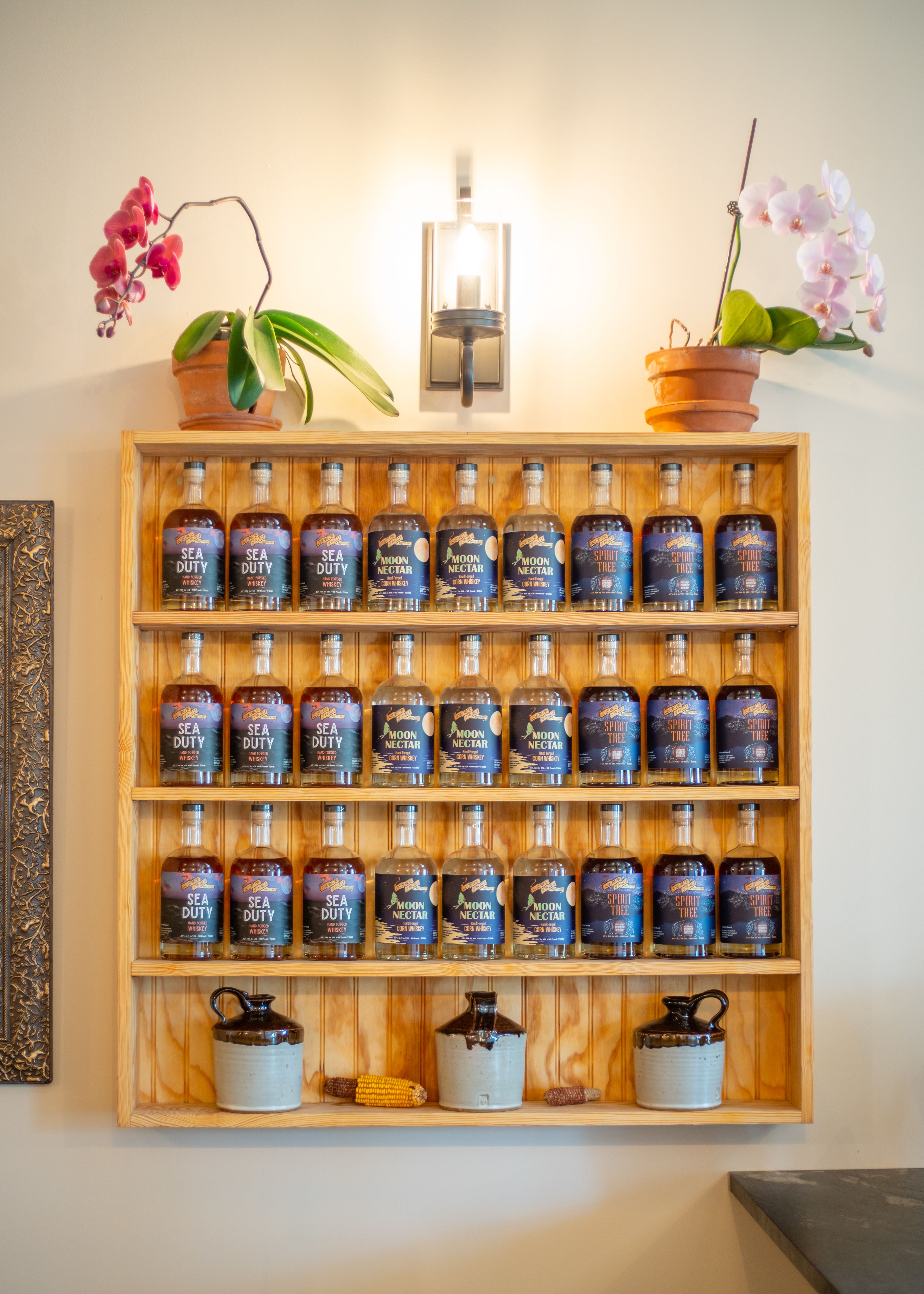 A zoomed-out view of whiskey offerings at Soldier of the Sea, lined up on a shelf with orchids and a lamp on top