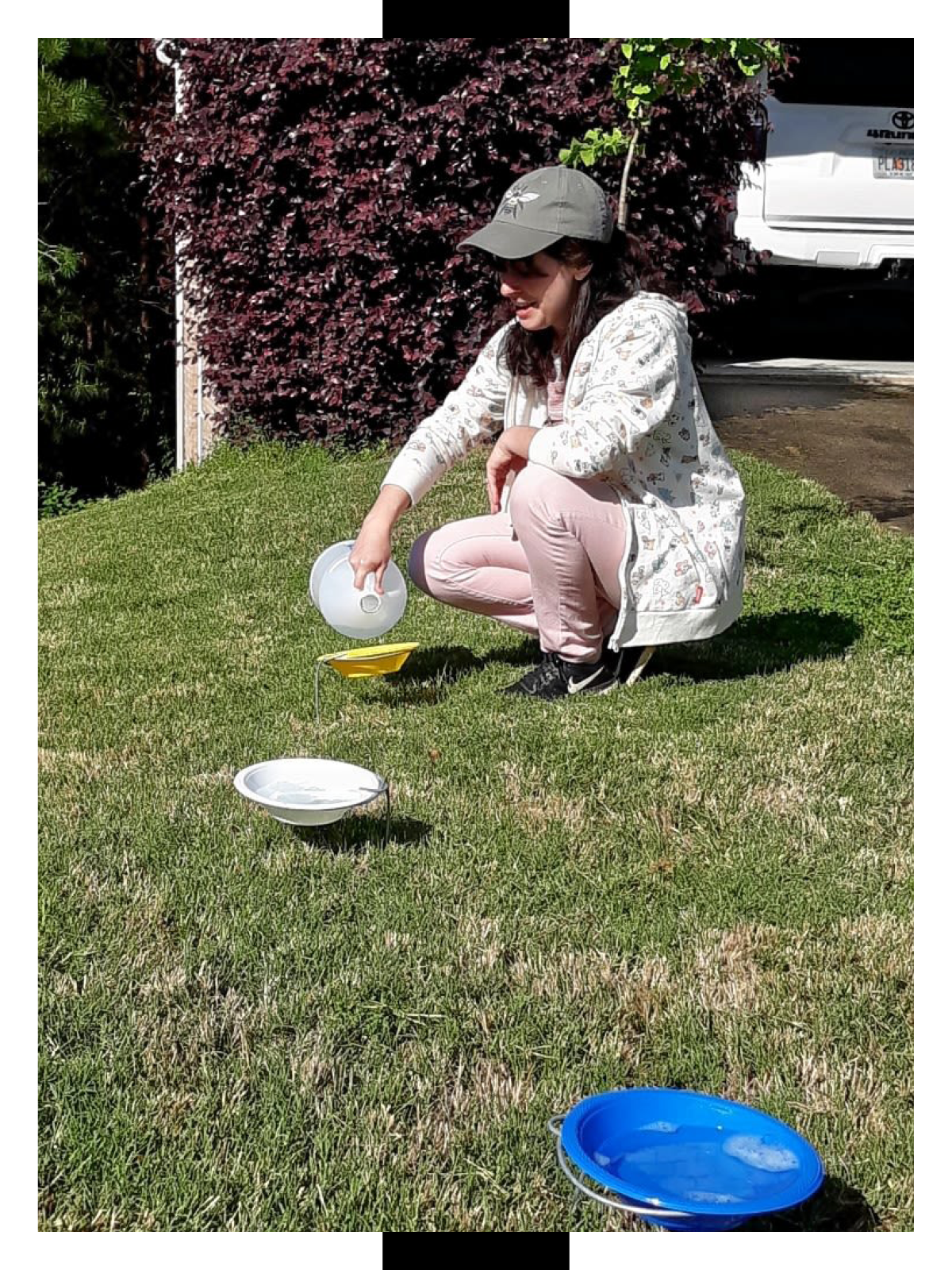 Amy Janvier is squatting while pouring vinegar in different colored bowls in a yard of a suburban neighborhood.