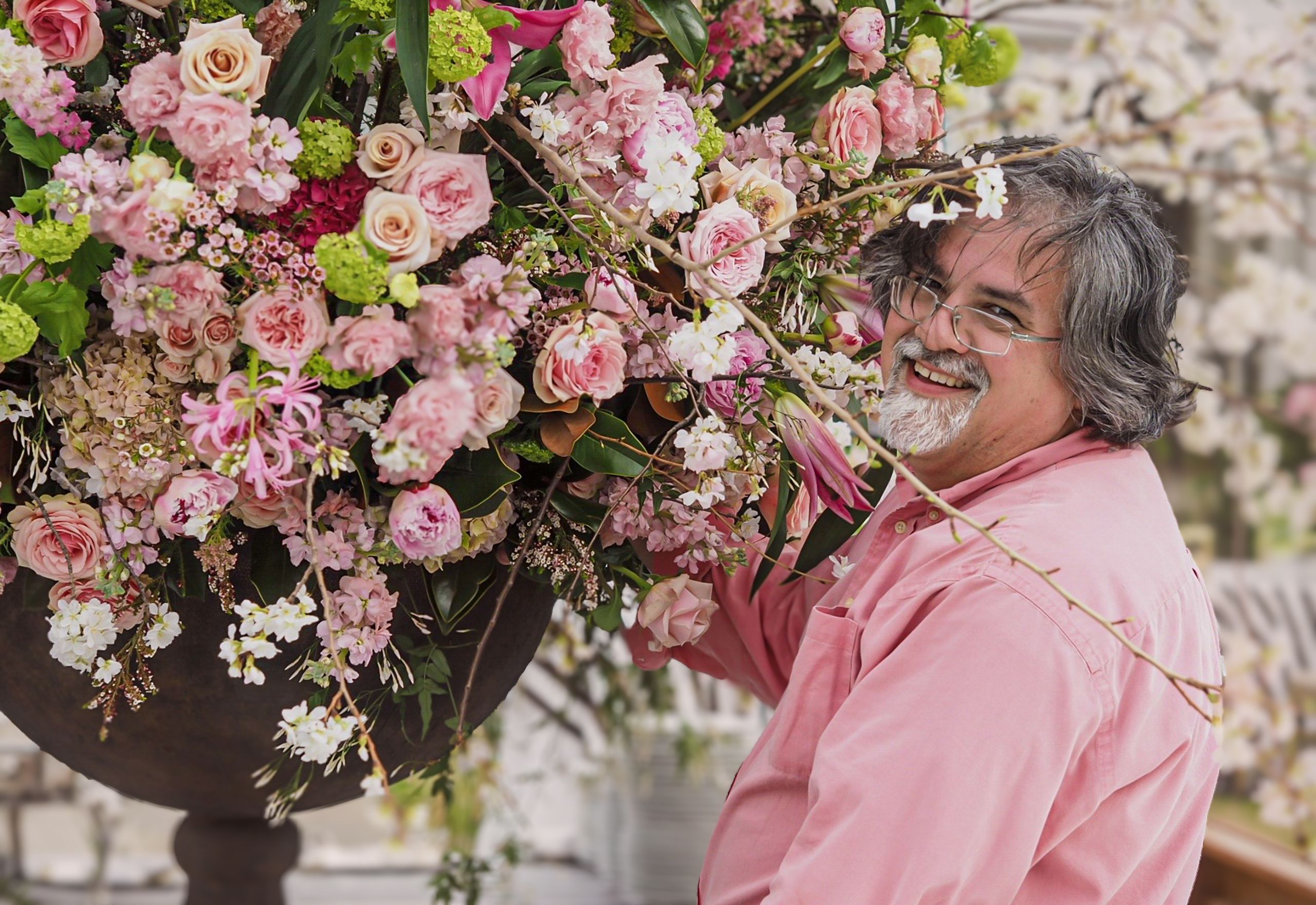 A man smiling beside a large floral arrangement of pink roses, white blossoms, and greenery.