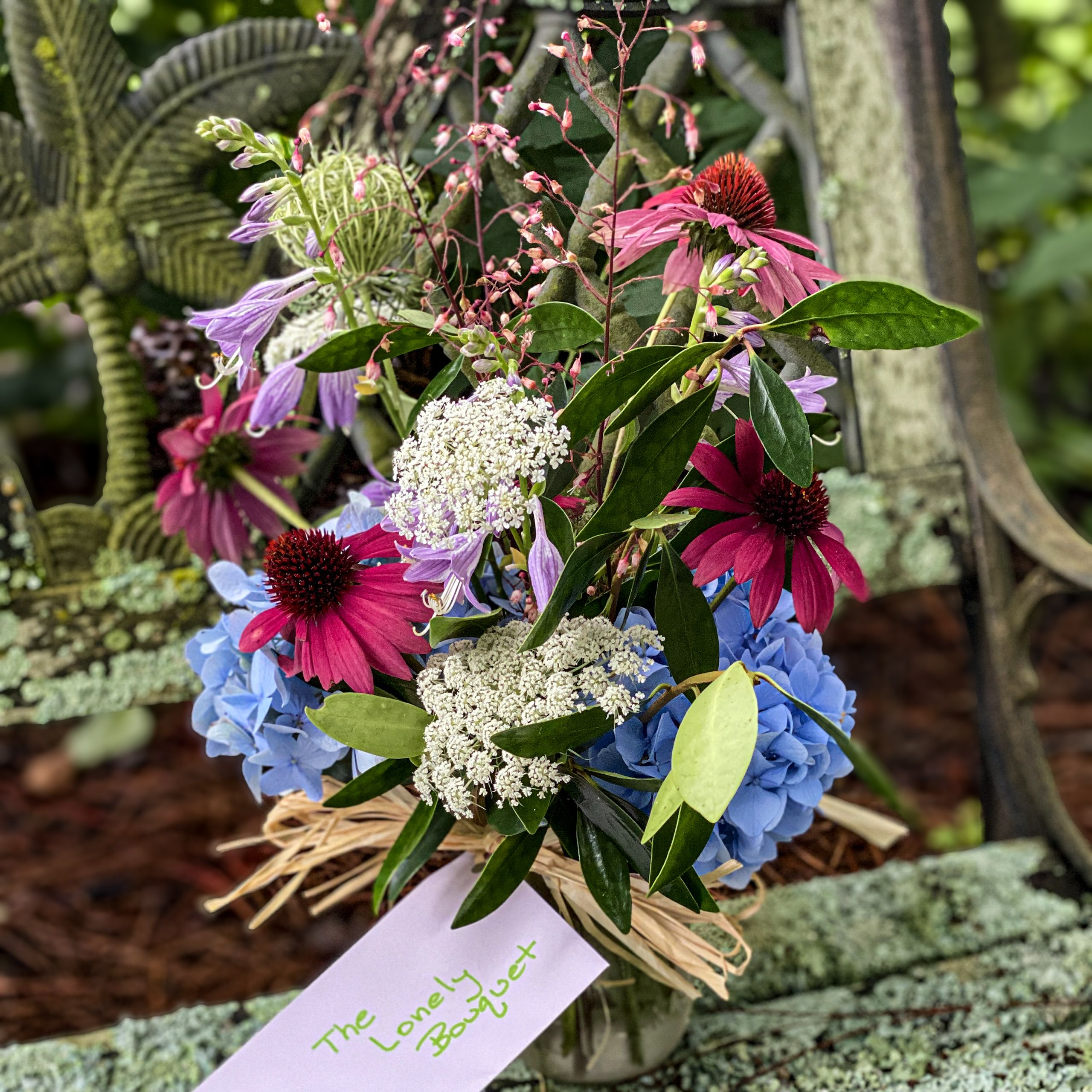 A bouquet of flowers including pink coneflowers, blue hydrangeas, white Queen Anne’s lace, and purple blooms.
