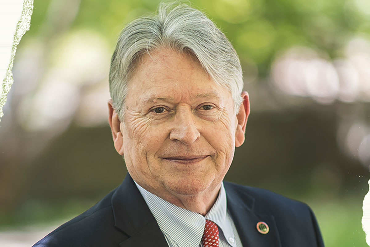 A man with silver hair wearing a blue blazer, white shirt and red tie smiles softly at the camera.
