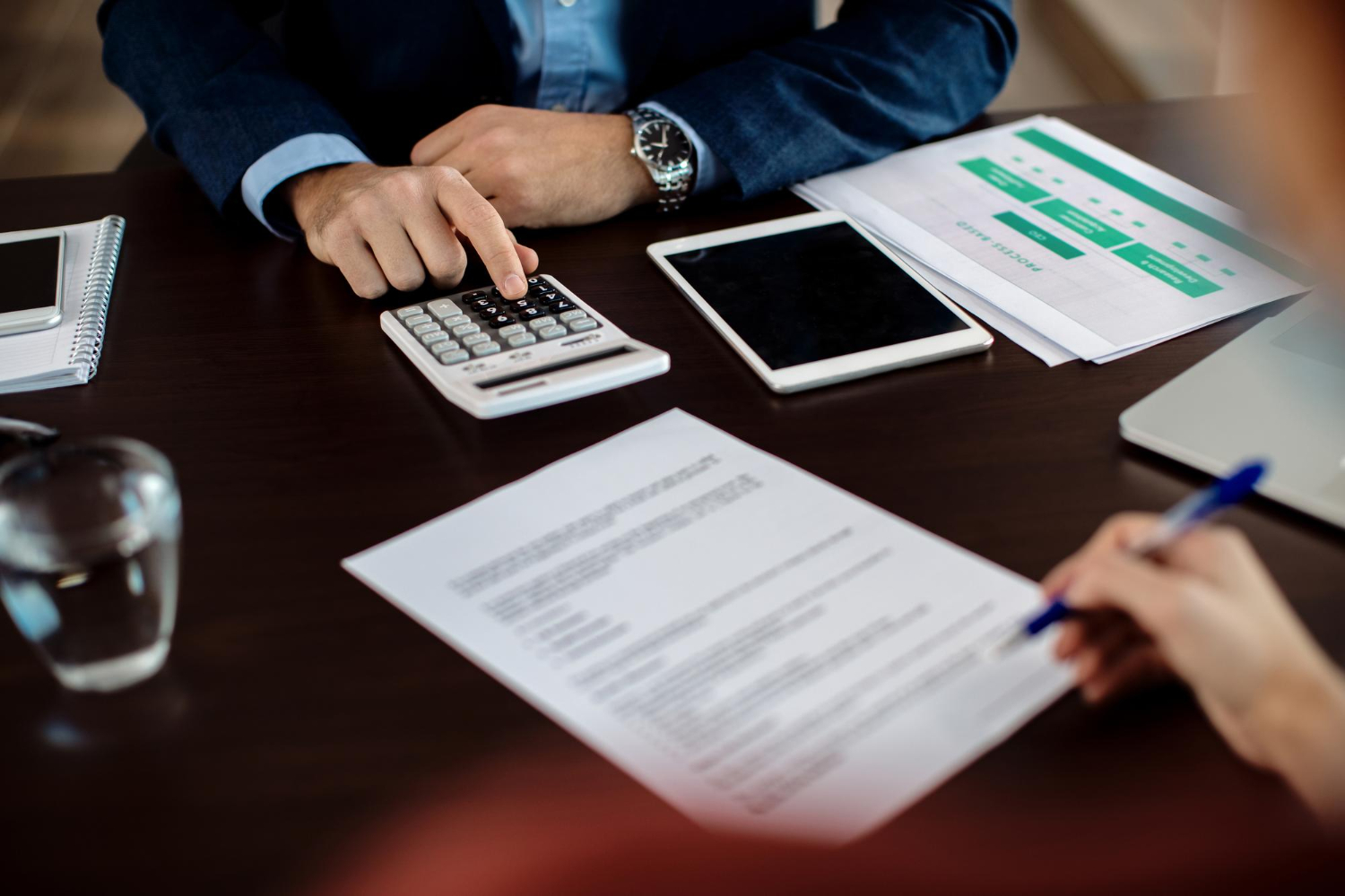 Closeup of agent using calculator while his client is signing a contract