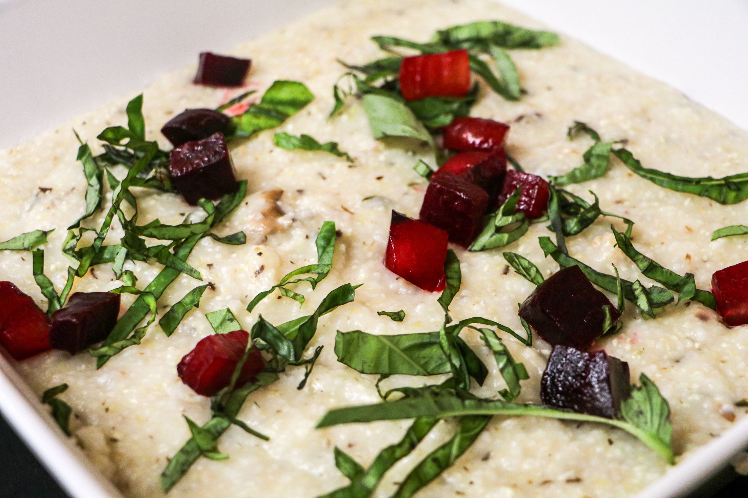 A close up image of white grits with chopped, red beets and basil on top.