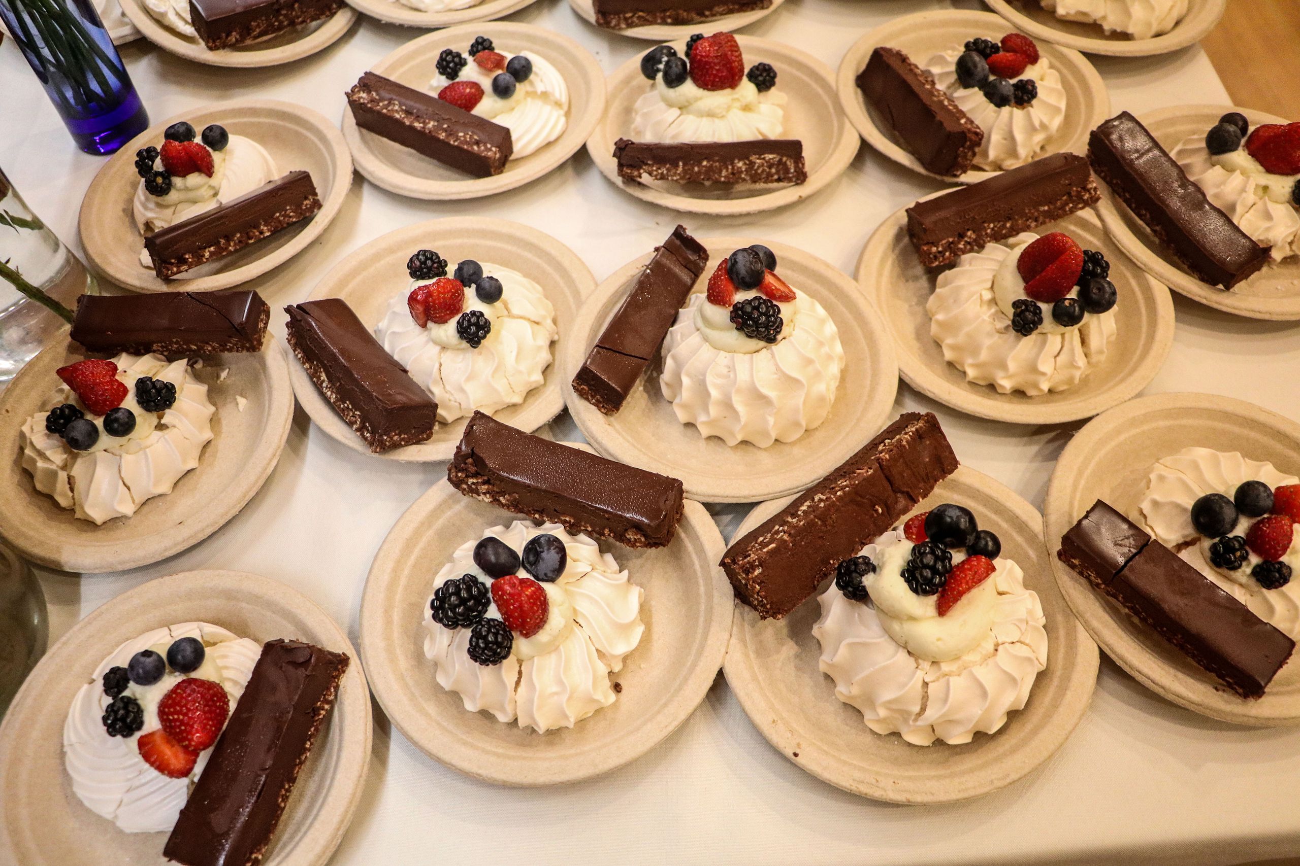 Plates of pavlova toped with mixed berries and a side bar of dark chocolate are lined up on a table.