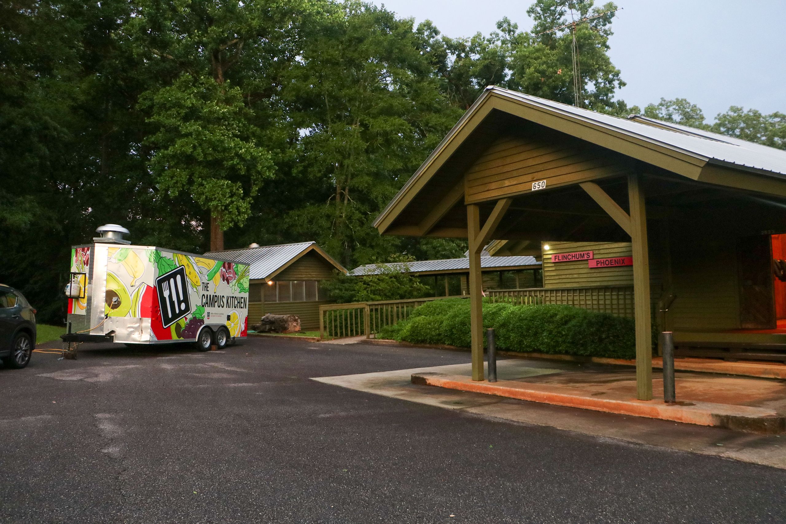 A food truck for Campus Kitchen sits outside Flinchum's Phoenix, where the gala is held. The wooden buildings have metal roofs against a forested backdrop.