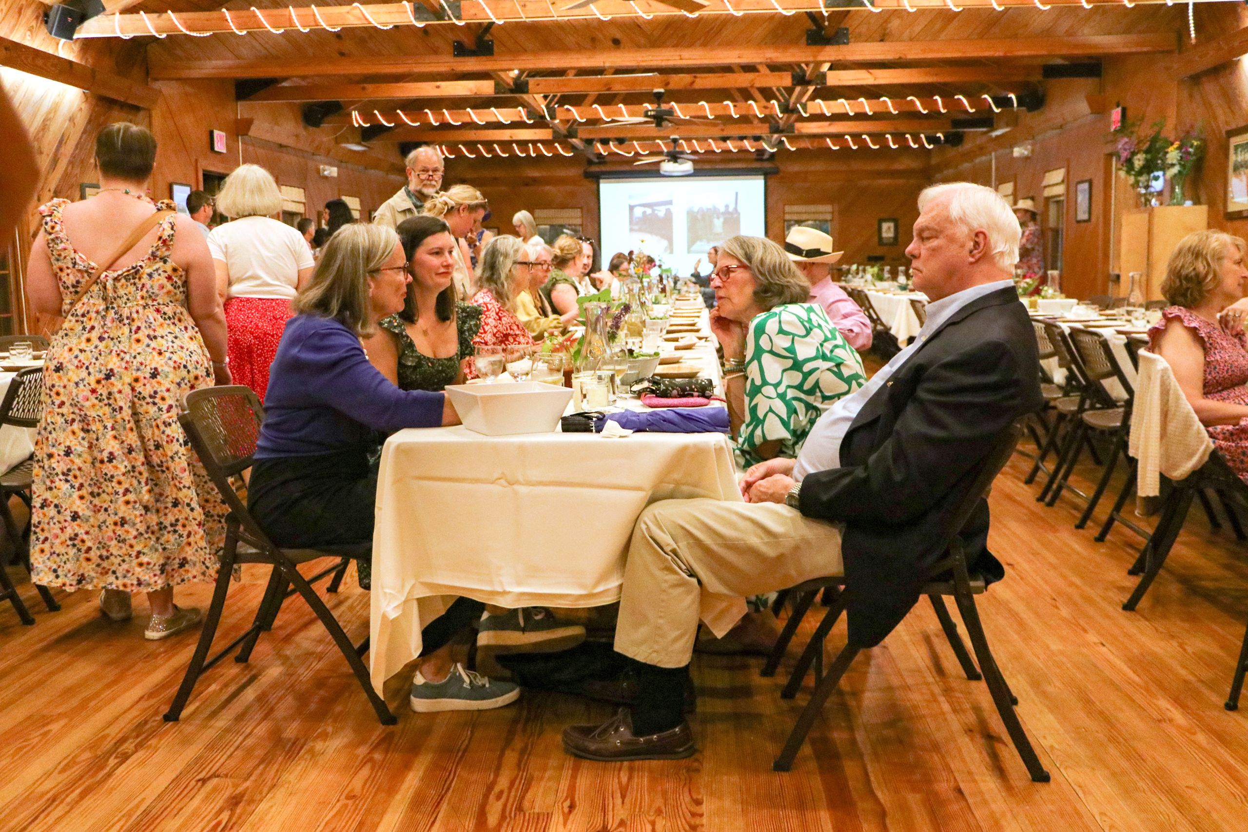 Looking down a long table, guests are intently talking amongst themselves as dinner is just beginning.