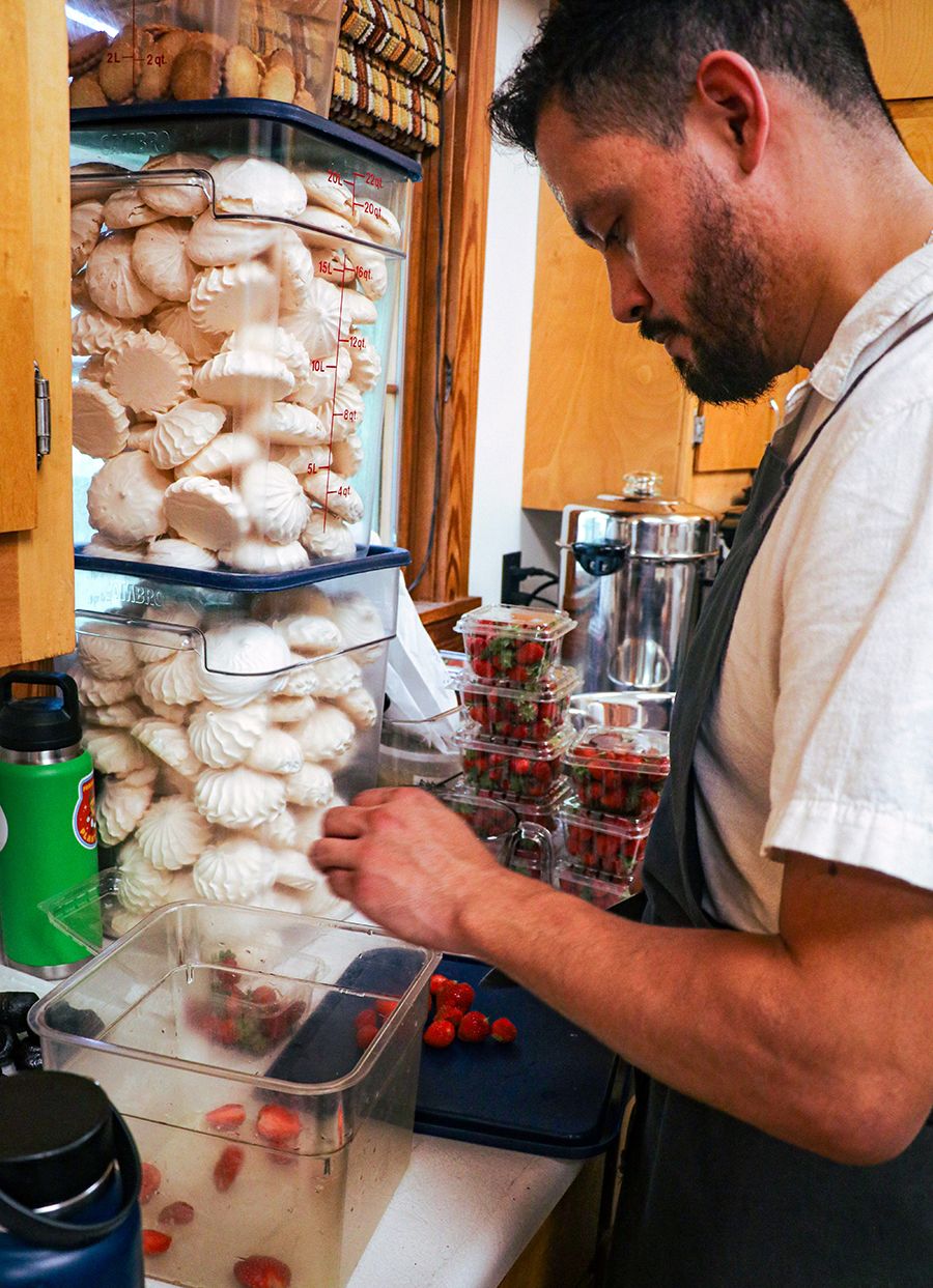 A chef chops red berries in preparation of the gala. Buckets of cream-colored pavlova are in the background.